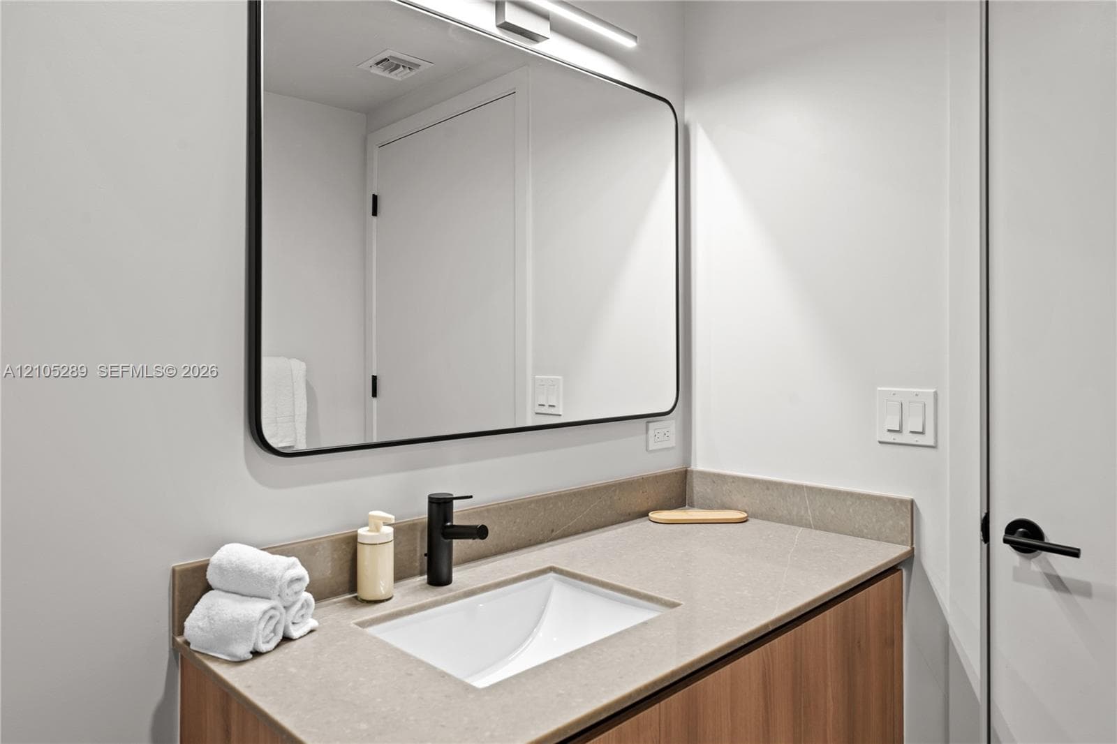 Modern vanity with an integrated sink, matte black faucet, and a wall-mounted mirror with overhead lighting
