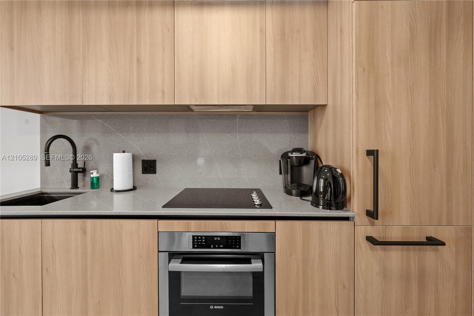 Integrated kitchen with wood-finish cabinetry, black hardware, a flush-mount cooktop, and a stainless-steel built-in oven