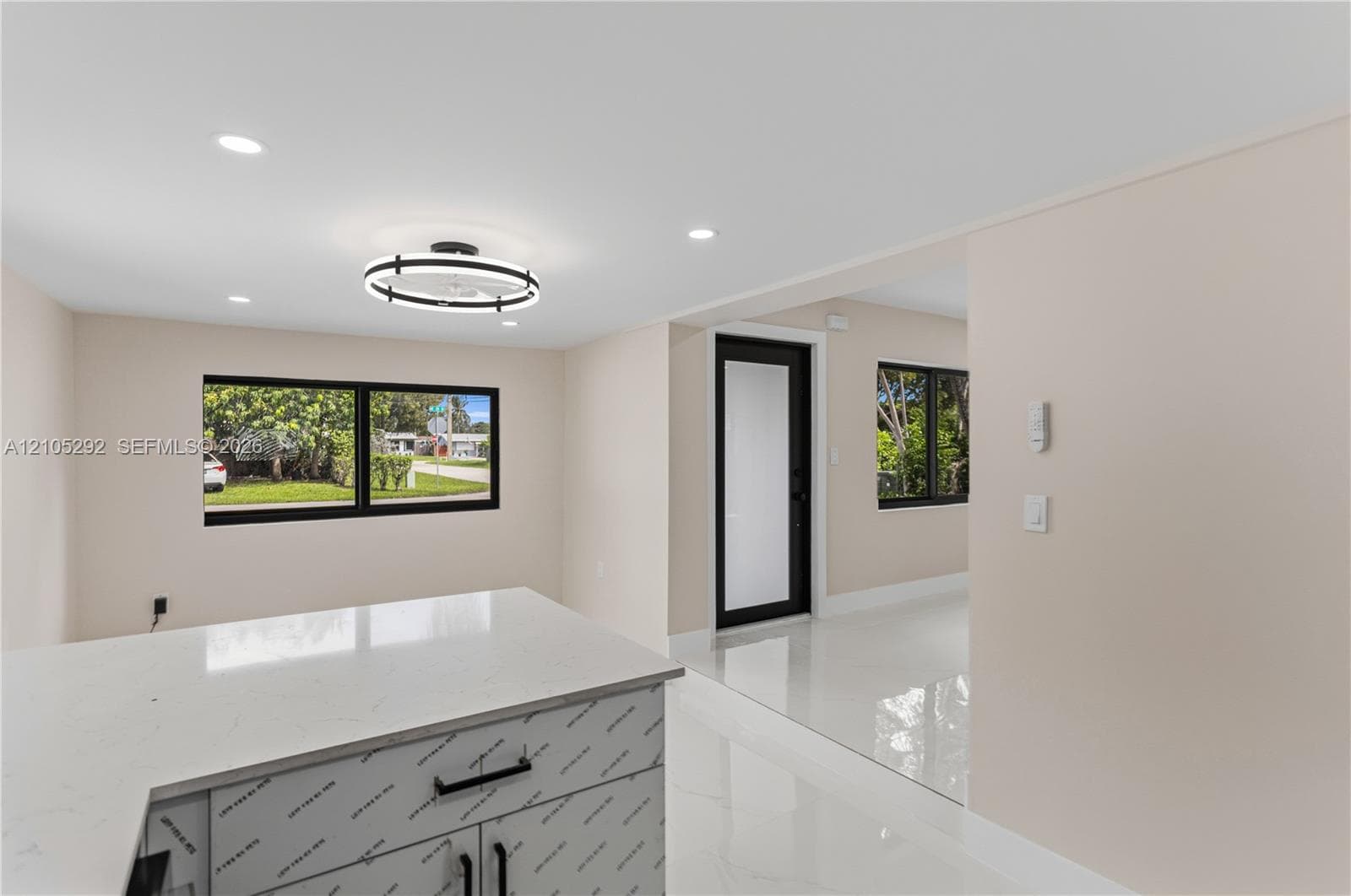 Sleek kitchen island with a light-colored countertop and dark hardware, complemented by recessed lighting and a modern circular light fixture