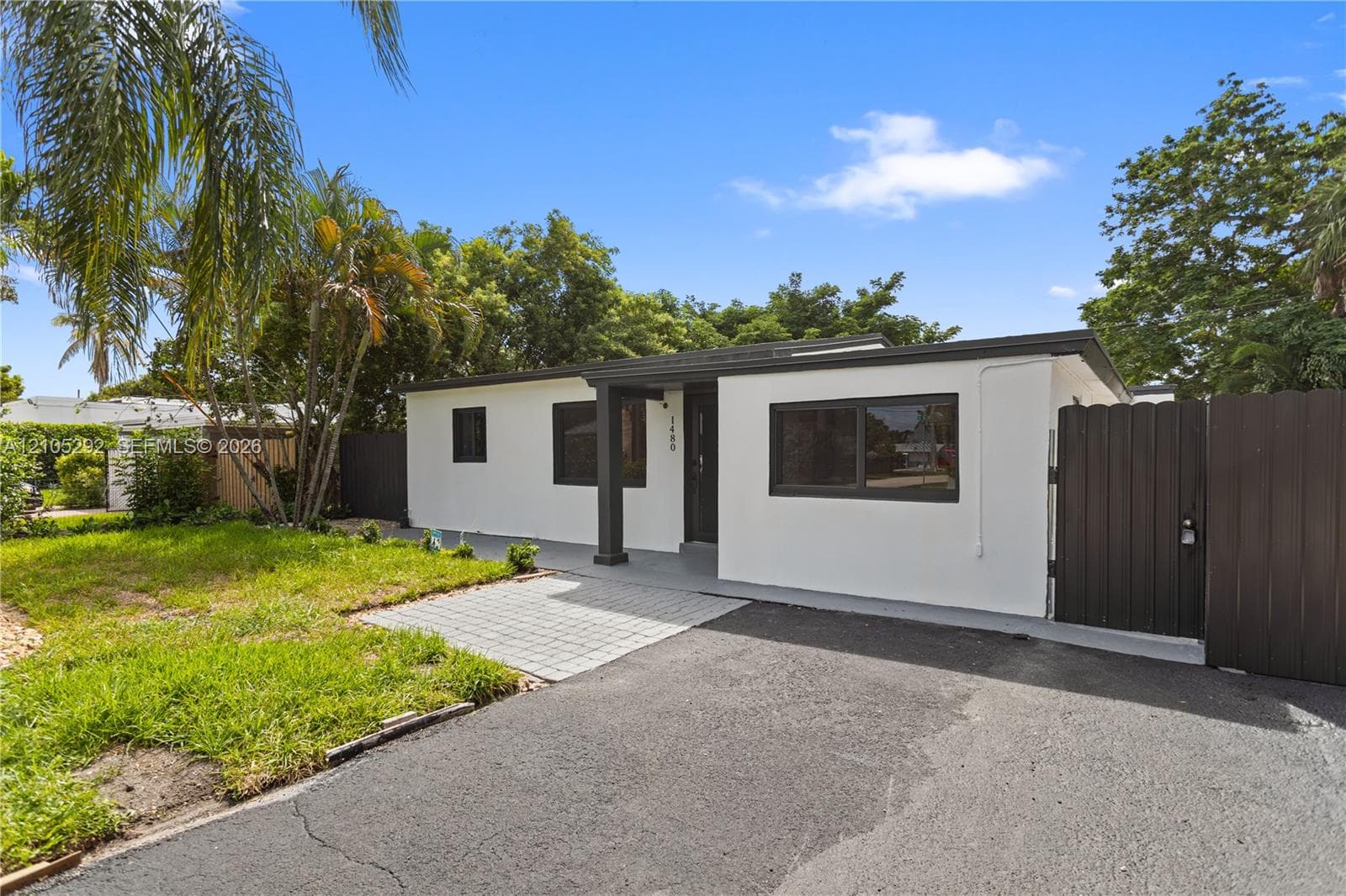 Single-story exterior with white stucco finish, dark trim windows, covered entry, gray paver walkway, and dark privacy fence