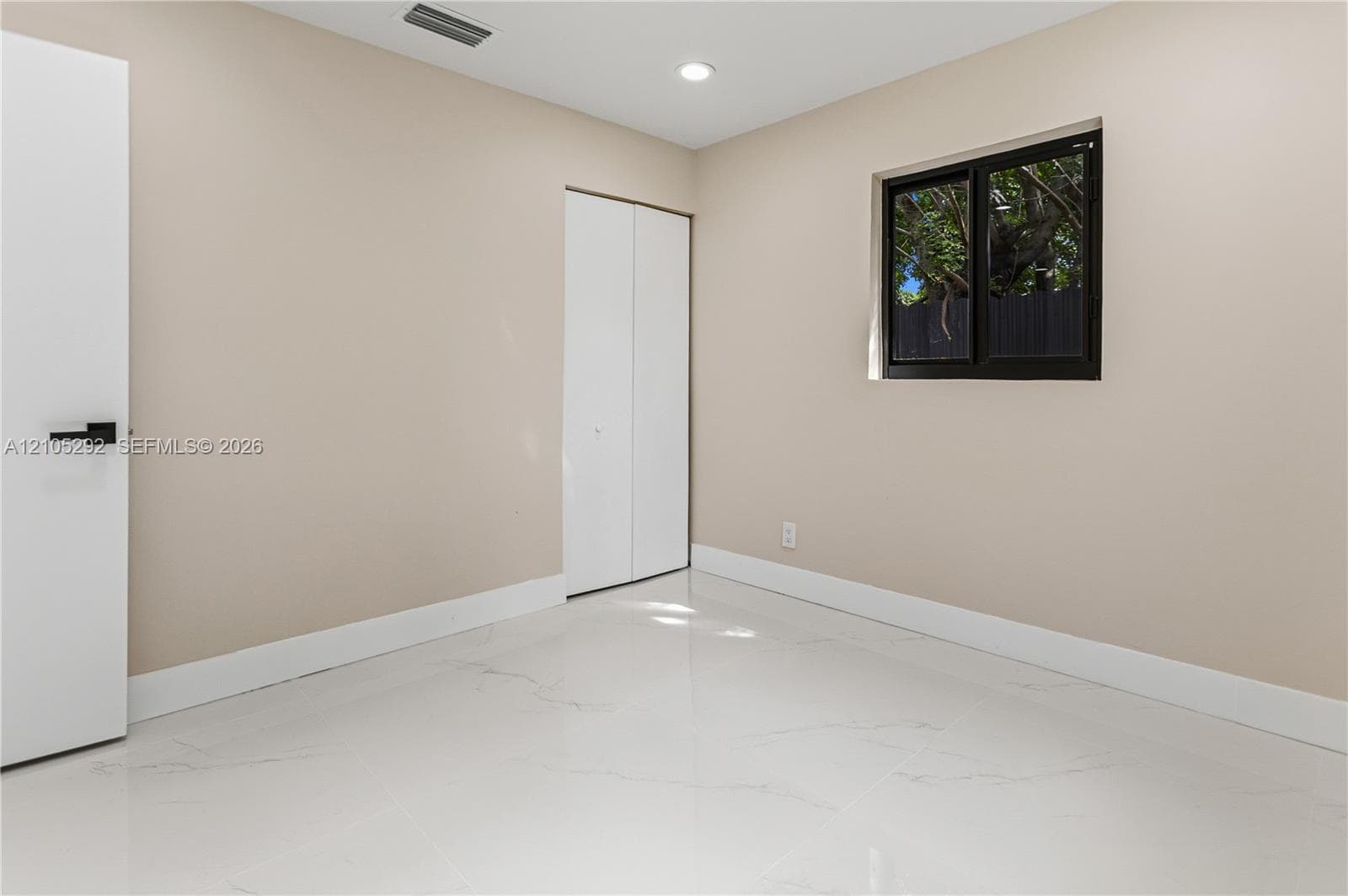 Bright, open room featuring pristine light-finish flooring, neutral beige walls, recessed ceiling lighting, and a framed window with natural light