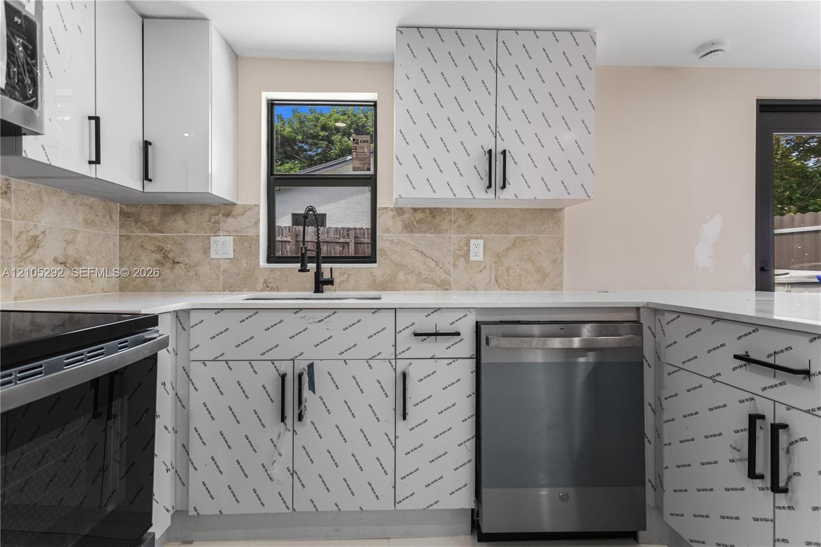 White cabinetry with black hardware, stone-finish backsplash, stainless steel appliances, white countertops, and a black sink faucet