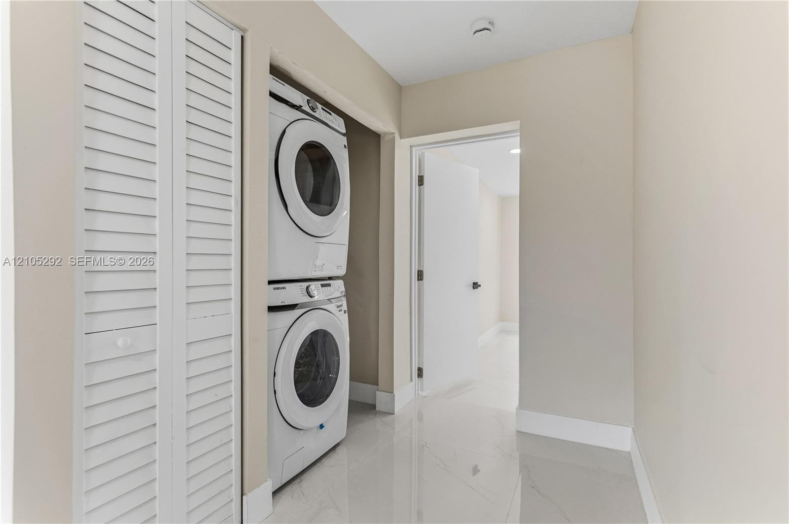 Laundry closet featuring a stacked washer and dryer, white louvered bifold doors, and a tiled floor
