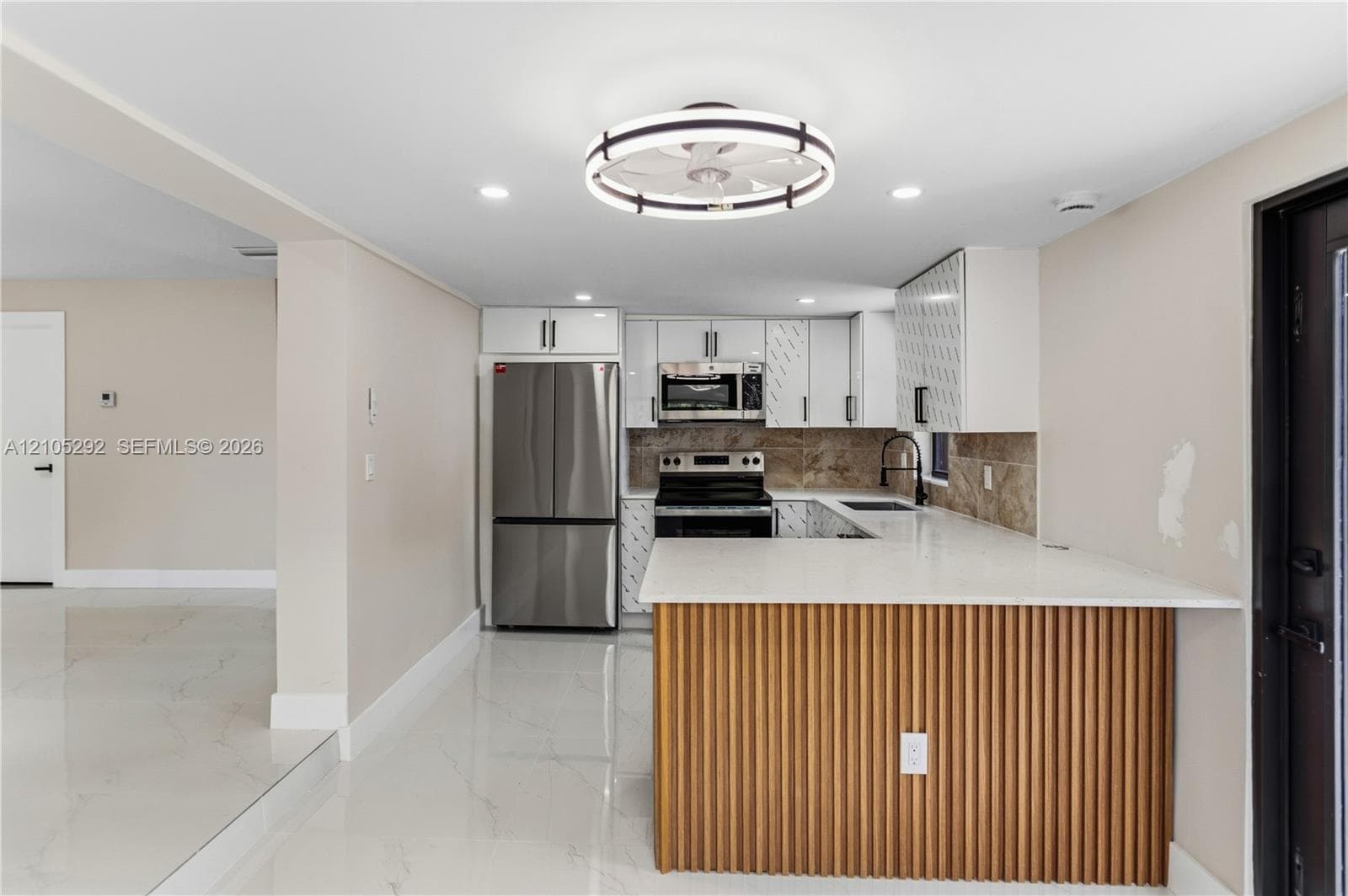 Kitchen with white cabinetry, stainless steel appliances, a tile backsplash, and a breakfast bar with a wood-slat base