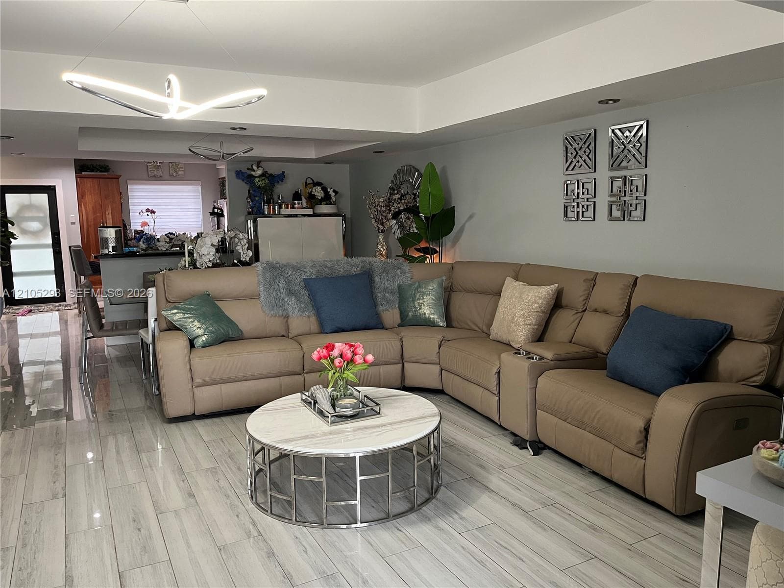 Open-concept interior featuring wood-finish tile flooring, recessed ceiling lighting, a modern geometric pendant light fixture, and crown molding