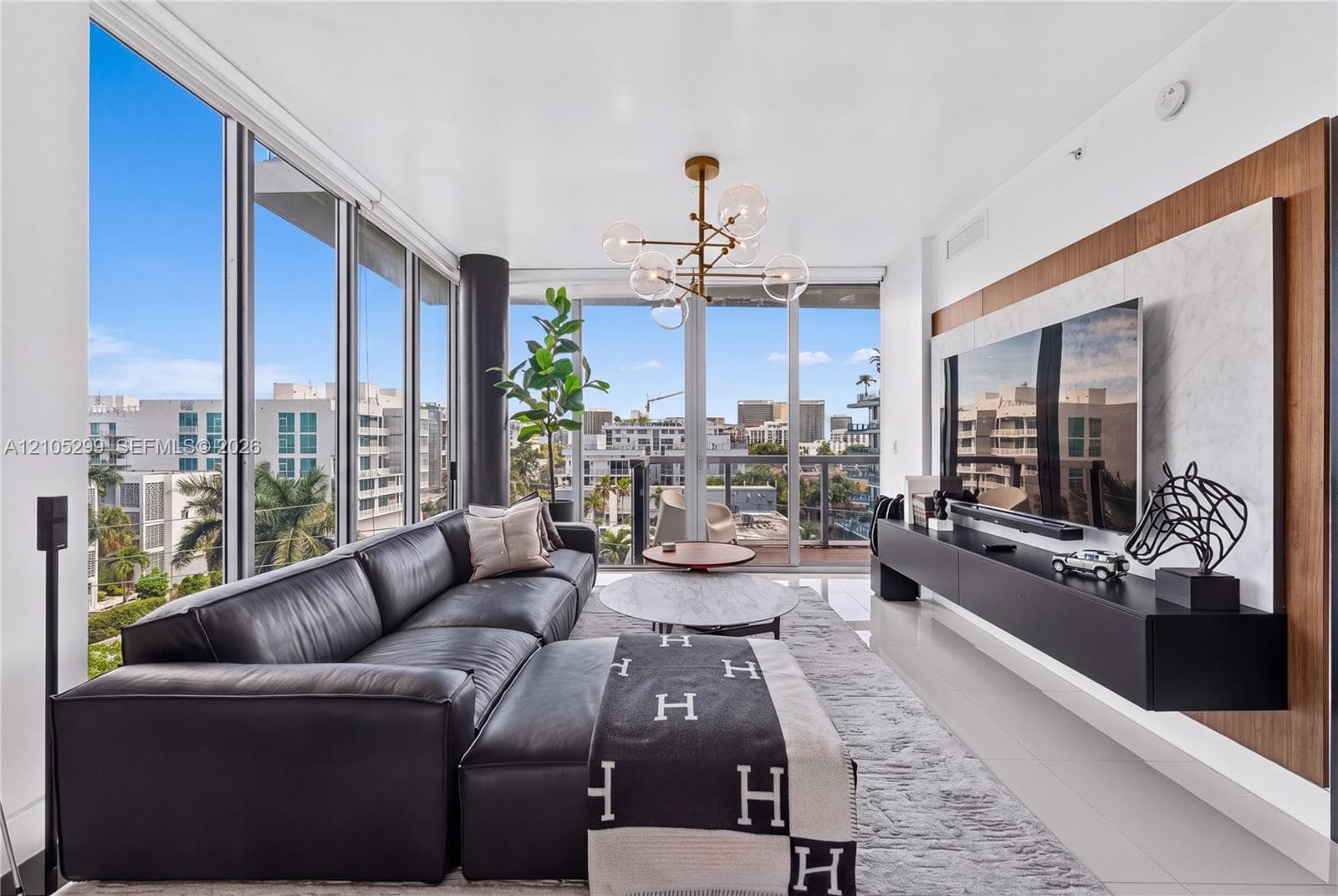 Floor-to-ceiling glass panels, contemporary chandelier, built-in entertainment console with wood-finish accent panel, and white tile flooring