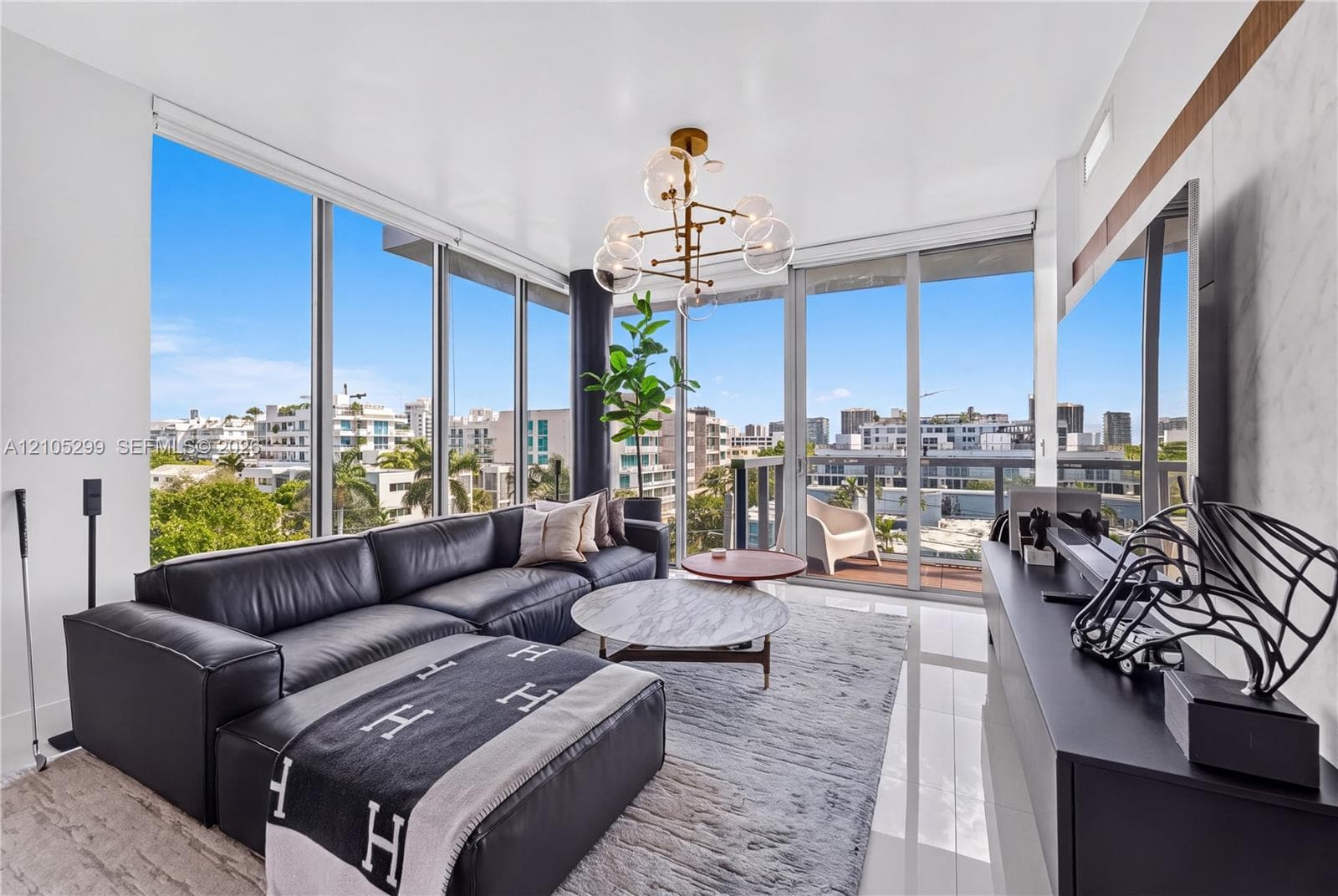 Floor-to-ceiling windows, polished tile flooring, modern chandelier, built-in media console, and a private balcony