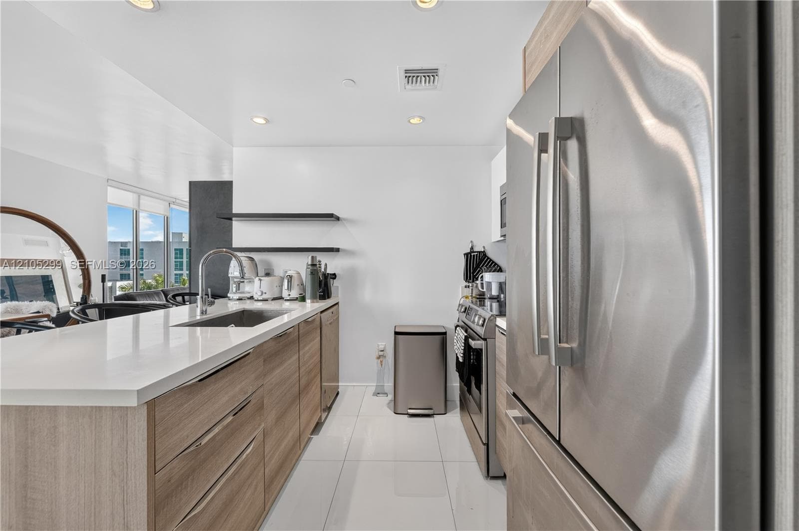 Kitchen featuring wood-finish cabinetry, white solid surface countertops, a stainless steel sink with a high-arch faucet, and stainless steel appliances