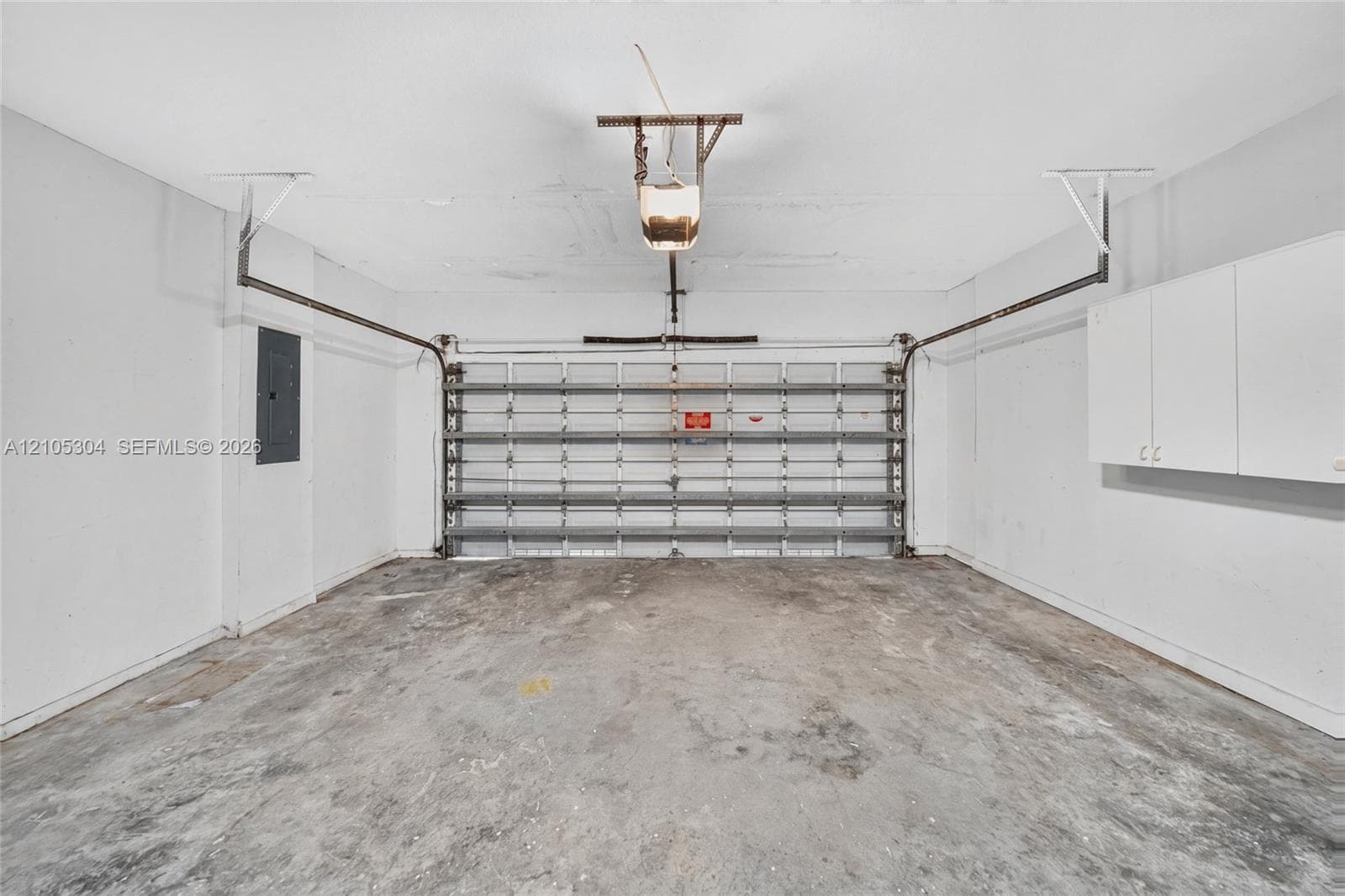 Two-car garage featuring a concrete floor, motorized sectional garage door, white wall-mounted storage cabinetry, and an electrical service panel