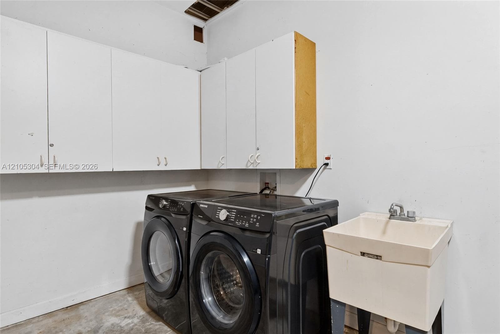 Wall-mounted white storage cabinetry, utility sink with chrome faucet, and dedicated laundry hookups