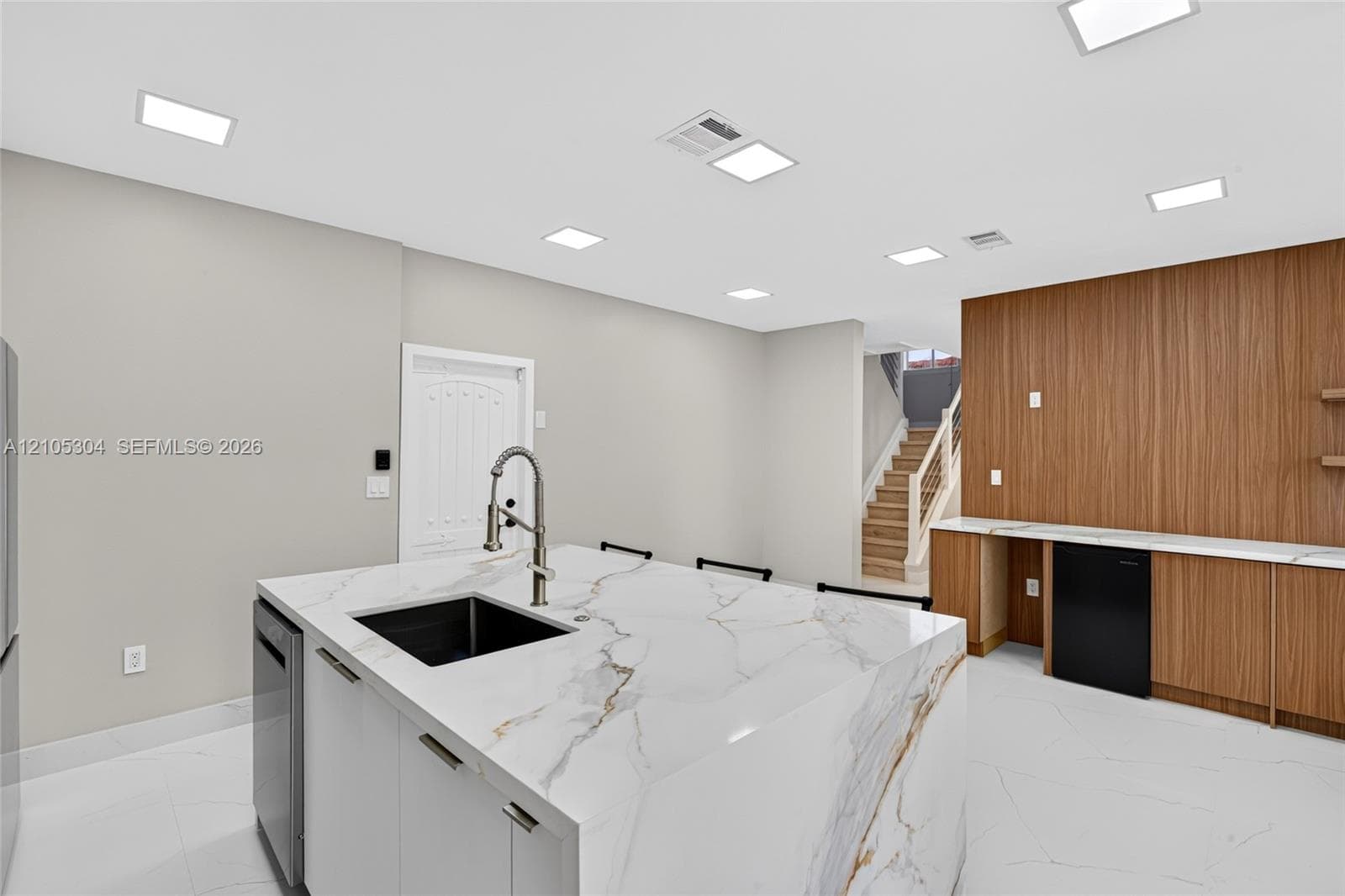 Kitchen island with stone-finish waterfall countertop and undermount sink, recessed lighting, wood-finish wall paneling, built-in cabinetry, and tile flooring