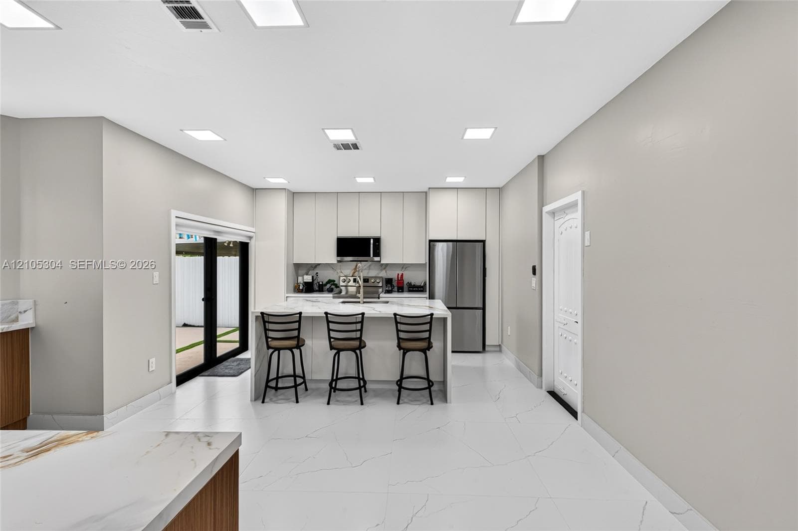 Kitchen featuring floor-to-ceiling cabinetry, a central island with a stone-surface countertop, stainless steel appliances, and large-format tile flooring with recessed lighting
