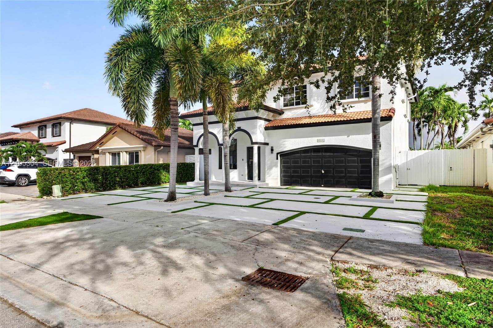 Two-story exterior featuring white stucco finish, arched entryways, multi-car garage with dark metal doors, tile roof, and a paved driveway with integrated turf grid patterns