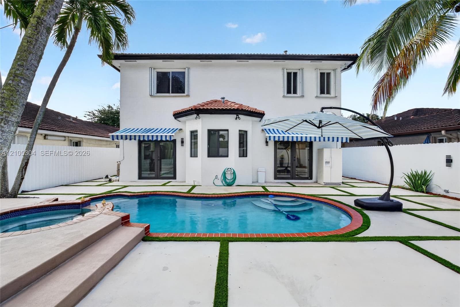 Stucco exterior featuring a pool and elevated spa with brick coping, concrete paver patio with turf joints, and retractable fabric awnings