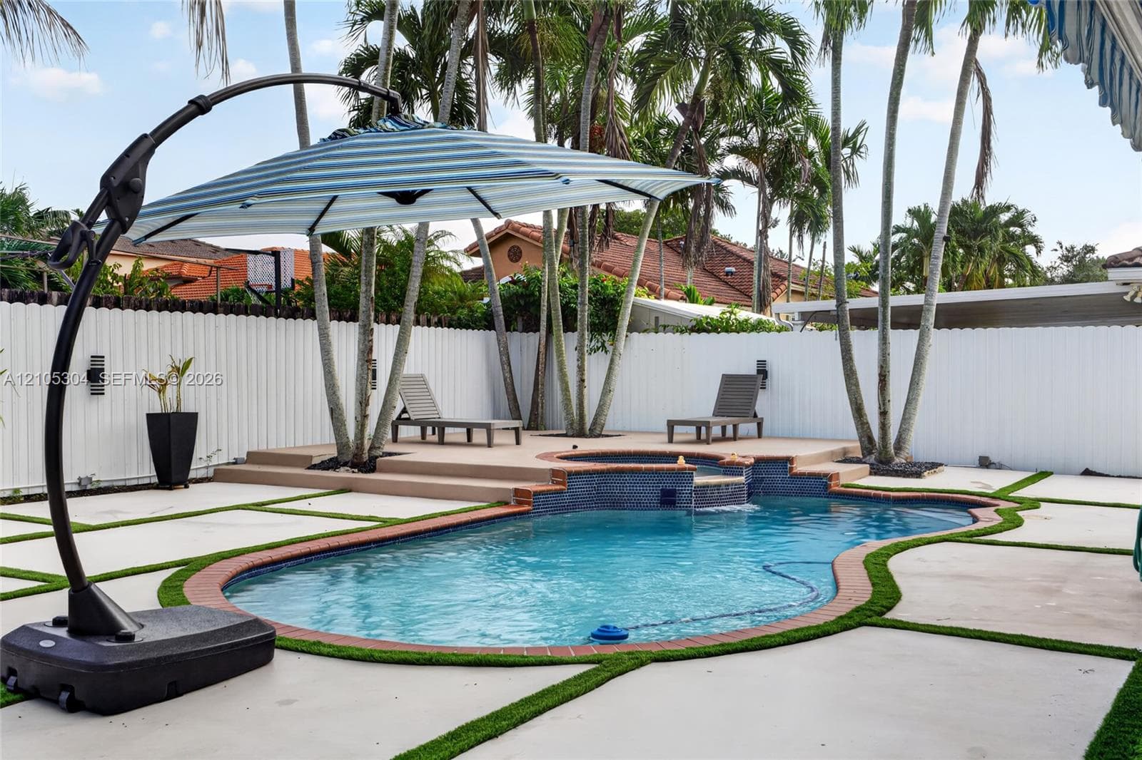 Backyard featuring a custom-shaped swimming pool with a tiered tile spa, concrete paver patio with turf detailing, and a perimeter privacy fence