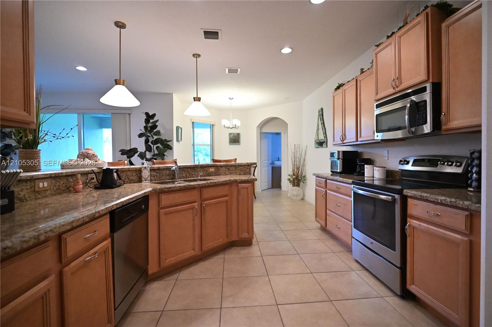 Kitchen featuring wood cabinetry, stainless steel appliances, granite countertops, and tile flooring