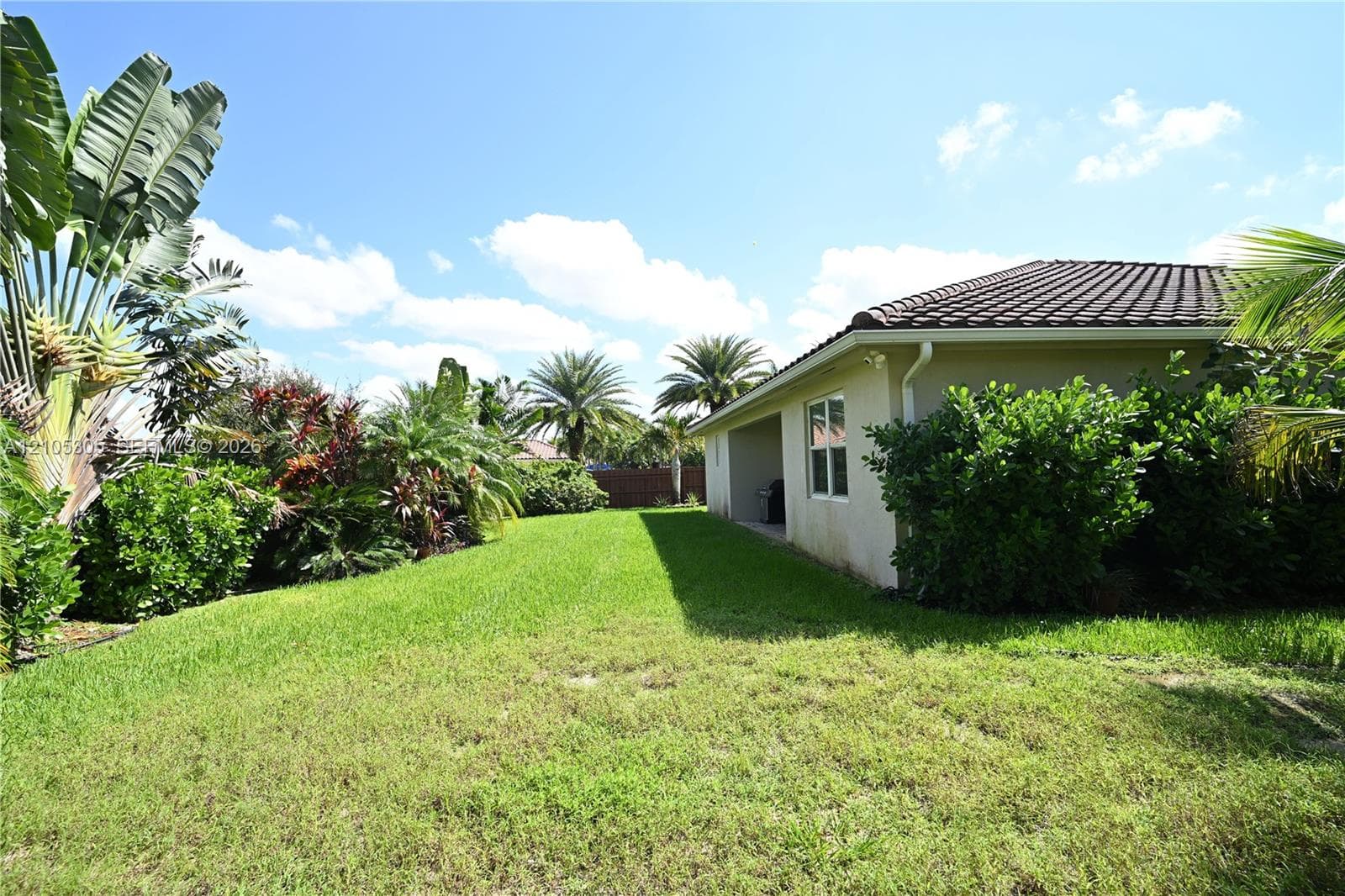 Expansive grassy yard with mature tropical landscaping and established shrubs
