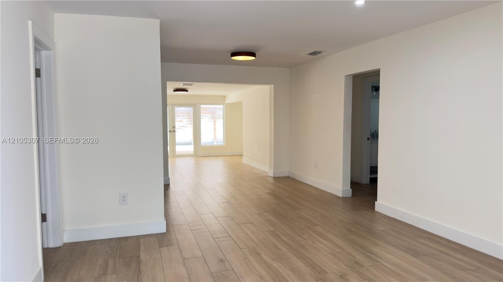 Interior space featuring wood-finish flooring, crisp white walls, flush-mount ceiling lighting, and multi-pane glass doors