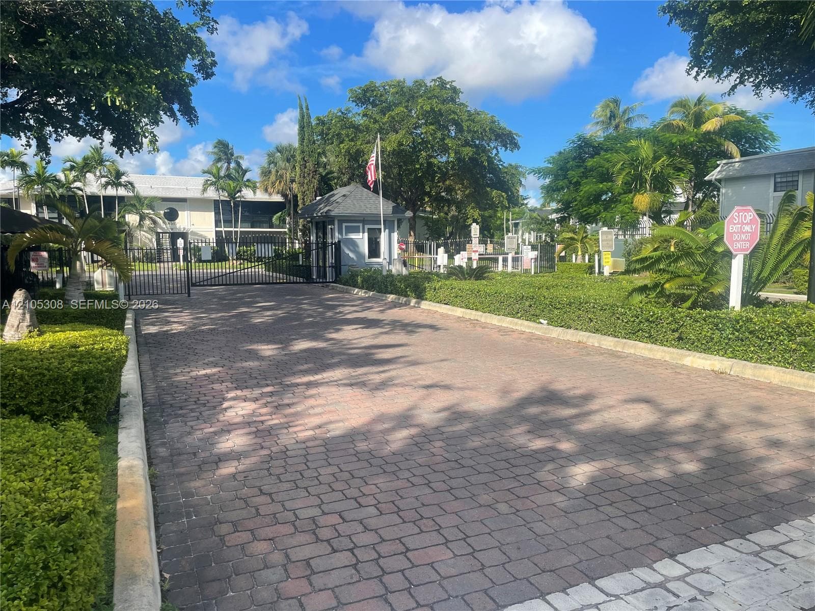 Gated entry featuring paver driveway, security gate, guard booth, and manicured landscaping