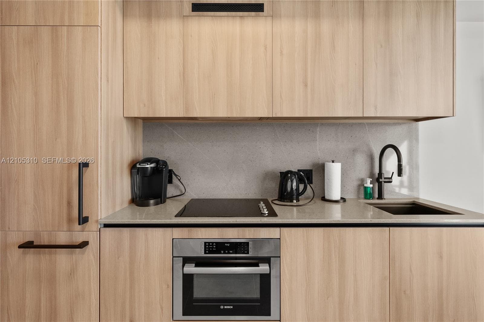 Kitchenette with integrated refrigerator, light wood-finish cabinetry, gray stone countertops, and a built-in oven