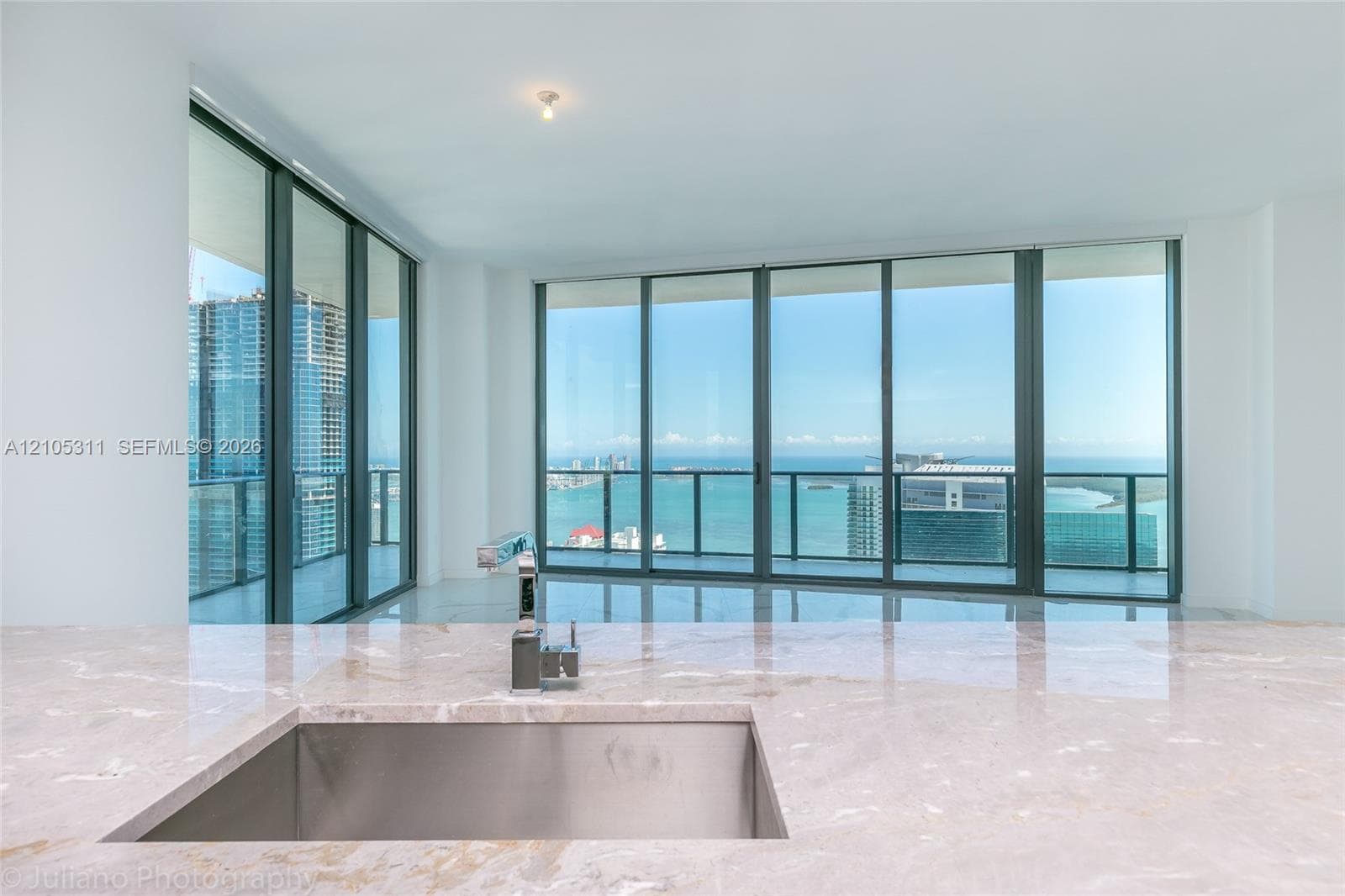 Expansive floor-to-ceiling windows, polished marble flooring, a stainless steel undermount sink, a contemporary faucet, and a stone countertop