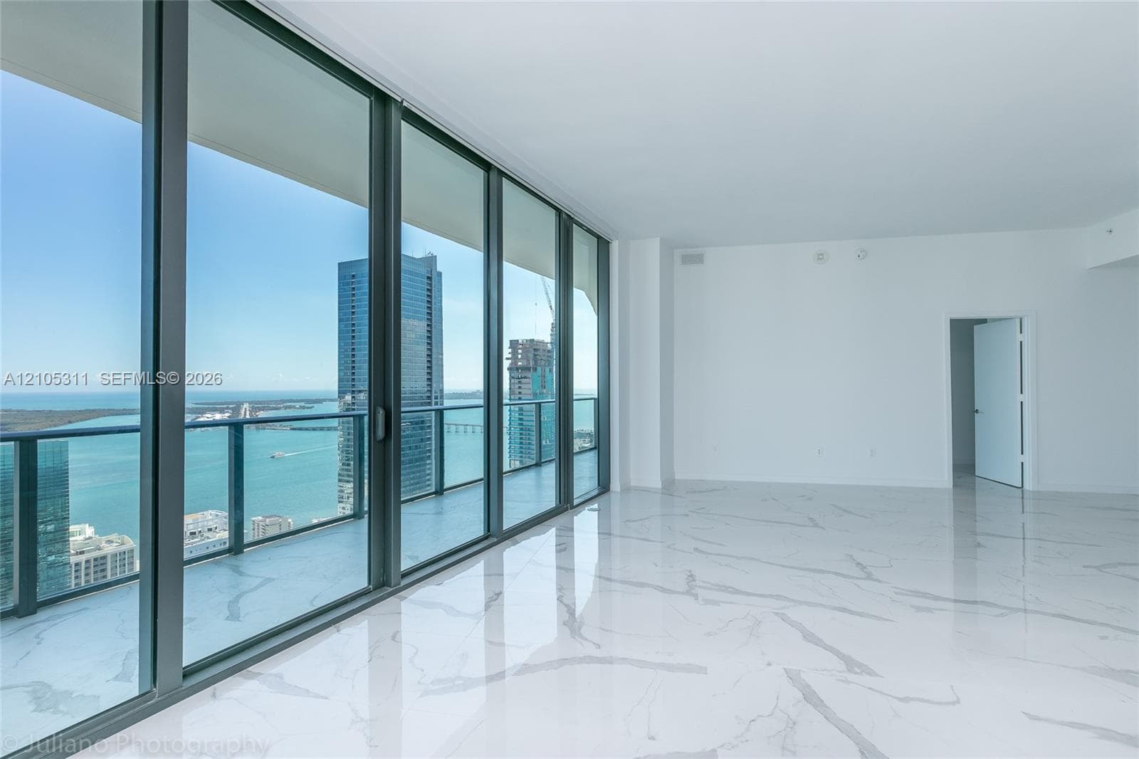 Expansive room featuring large format marble-look flooring, a full wall of floor-to-ceiling glass, and a balcony with a glass railing