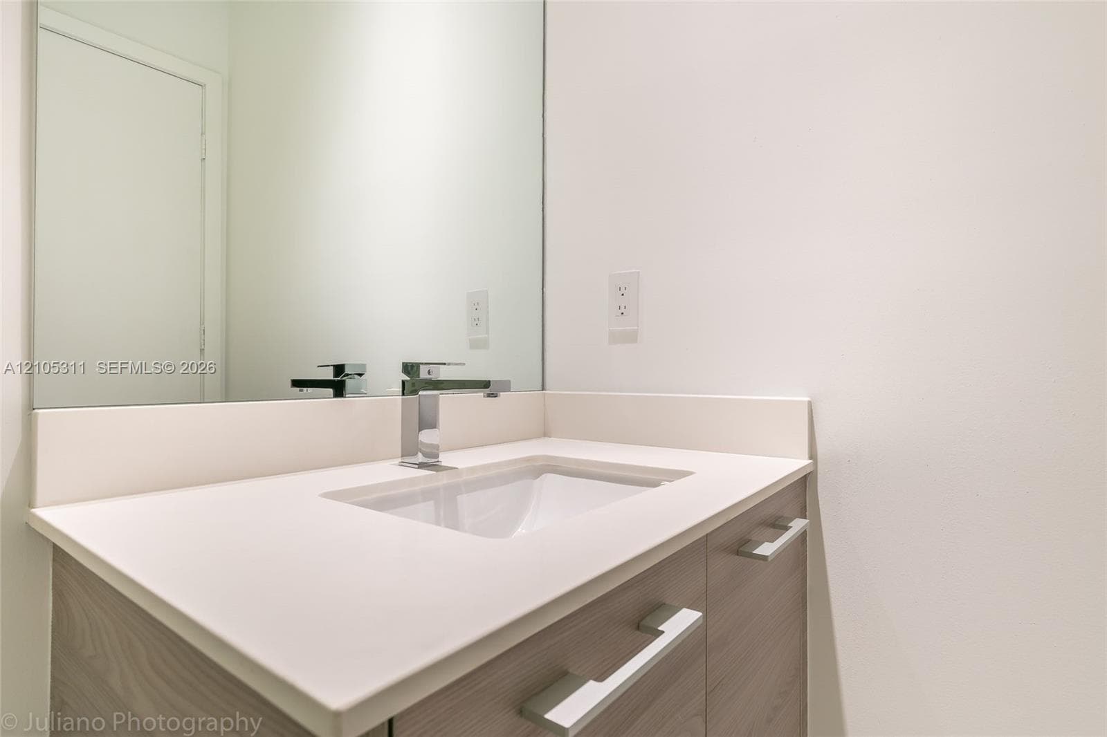 Modern vanity with wood-finish cabinetry, integrated sink, polished chrome faucet, and expansive mirror
