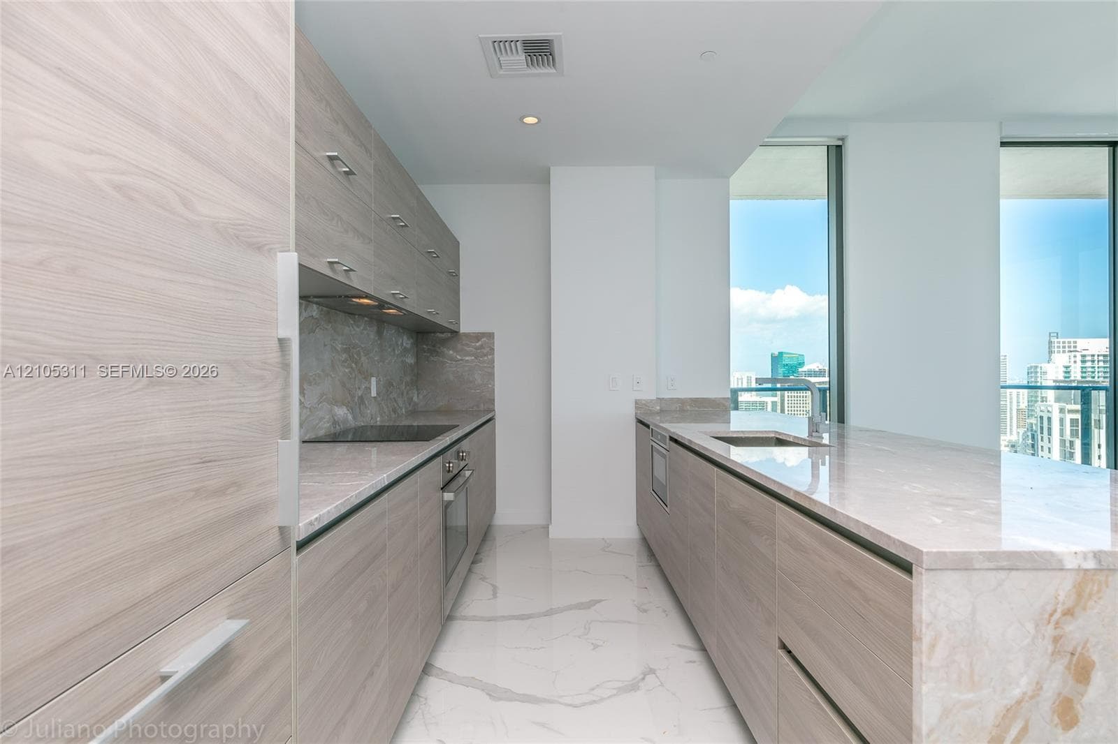 Modern galley kitchen featuring wood-finish cabinetry, integrated appliances, stone countertops, and a stone backsplash