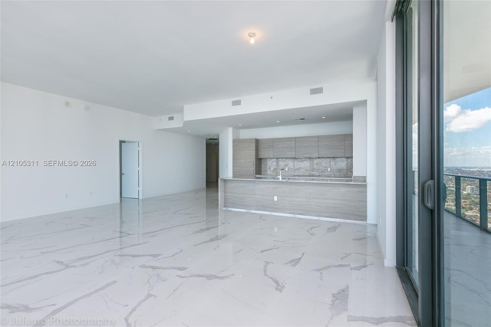 Expansive open-concept living area featuring large format tile flooring, a contemporary kitchen with flat-panel cabinetry, a kitchen island, and direct access to a private balcony