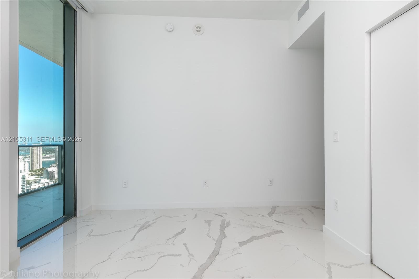 Large format tile flooring, floor-to-ceiling sliding glass doors, white walls, recessed lighting, and a cityscape backdrop