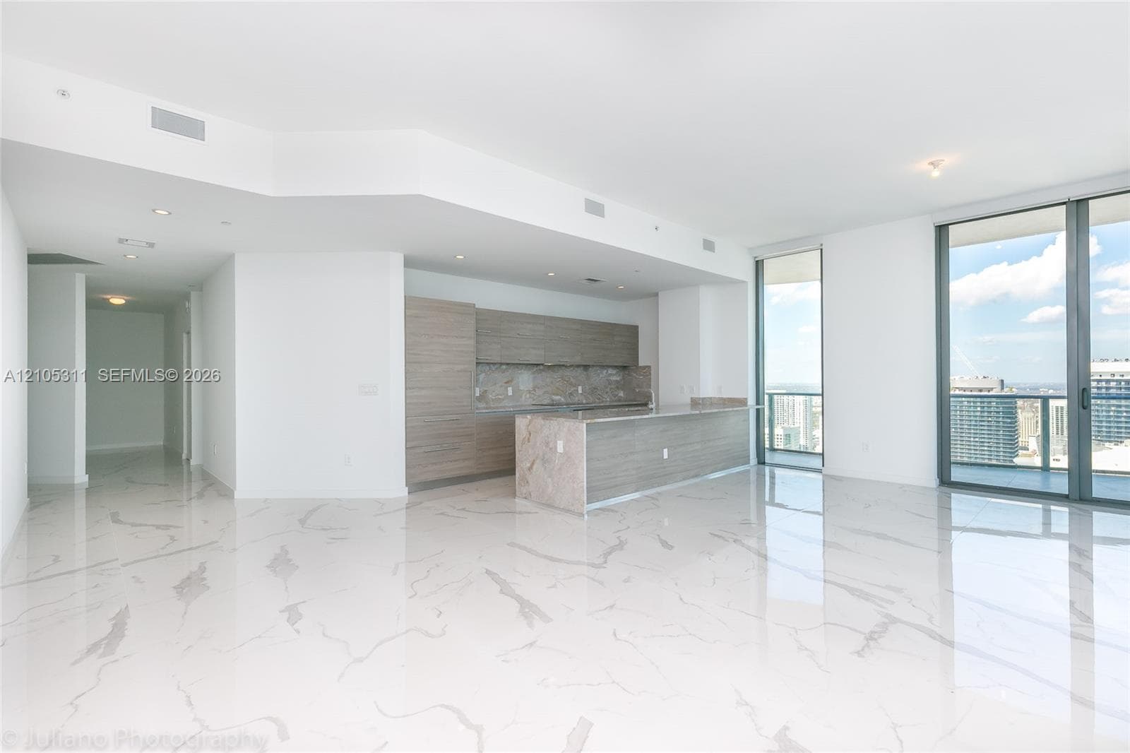 Open concept living space featuring white marble-look flooring, a kitchen island with a stone countertop, light wood-finish cabinetry, and large sliding glass doors