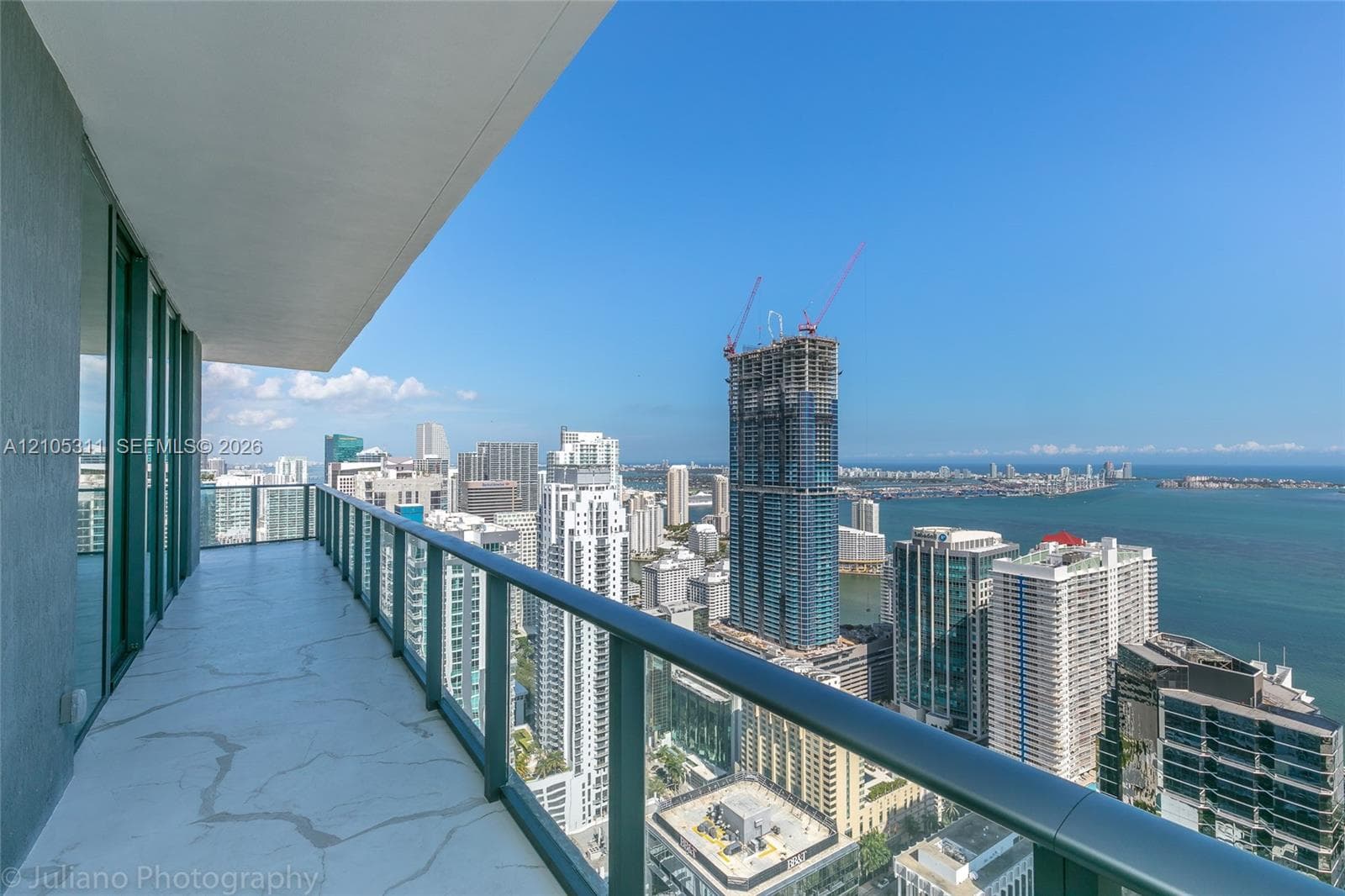 Expansive balcony with glass panel railing and tile flooring, offering a prominent city and water backdrop