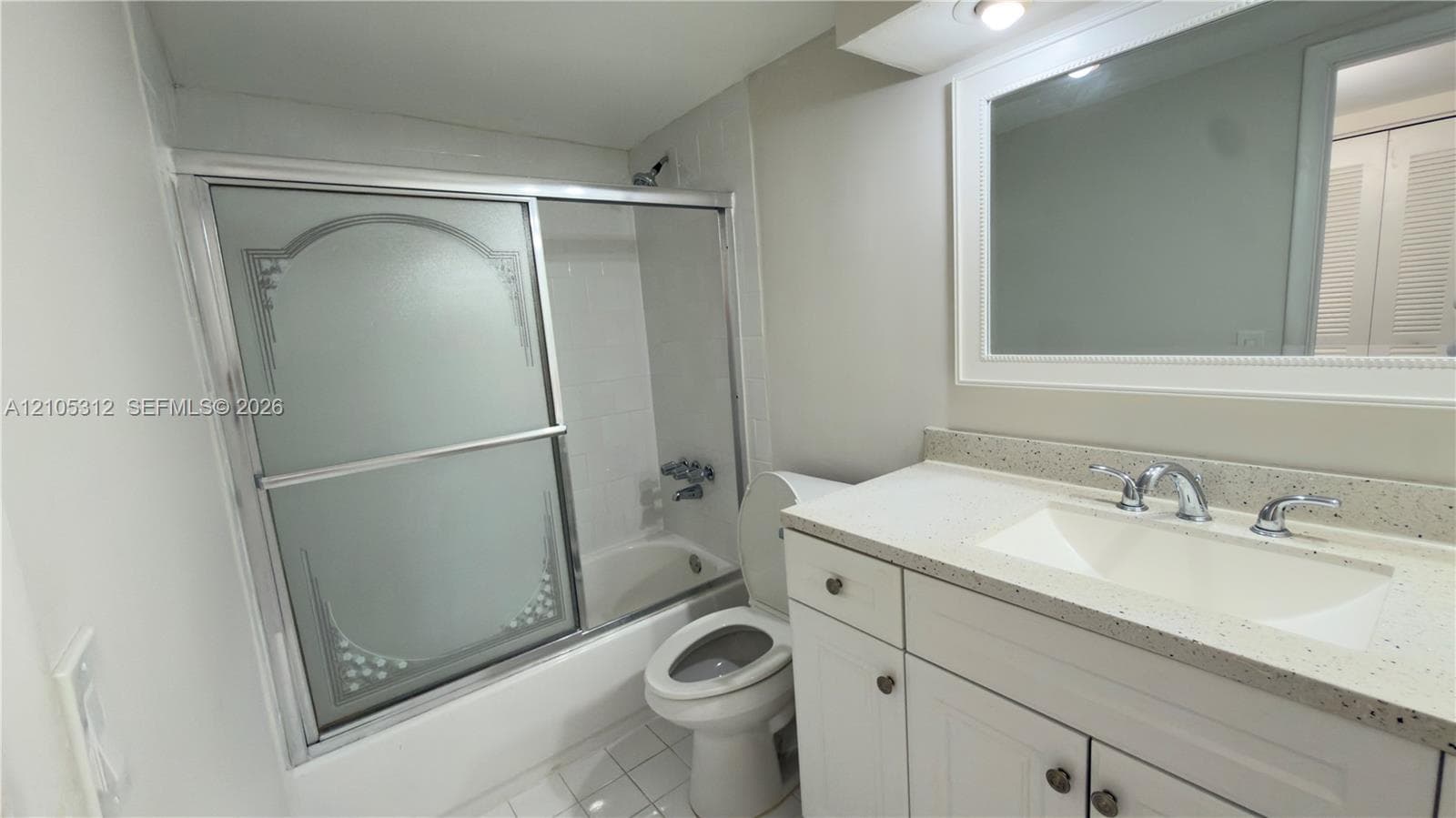 Bathroom featuring a white vanity cabinet with a speckled countertop, integrated sink with a chrome faucet, large framed wall mirror, and a shower-tub combination with sliding etched-glass doors