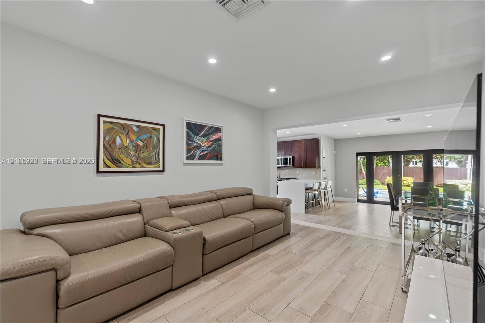 Recessed lighting, wood-finish flooring, cased opening to kitchen, kitchen with white island, dining area with glass doors to exterior