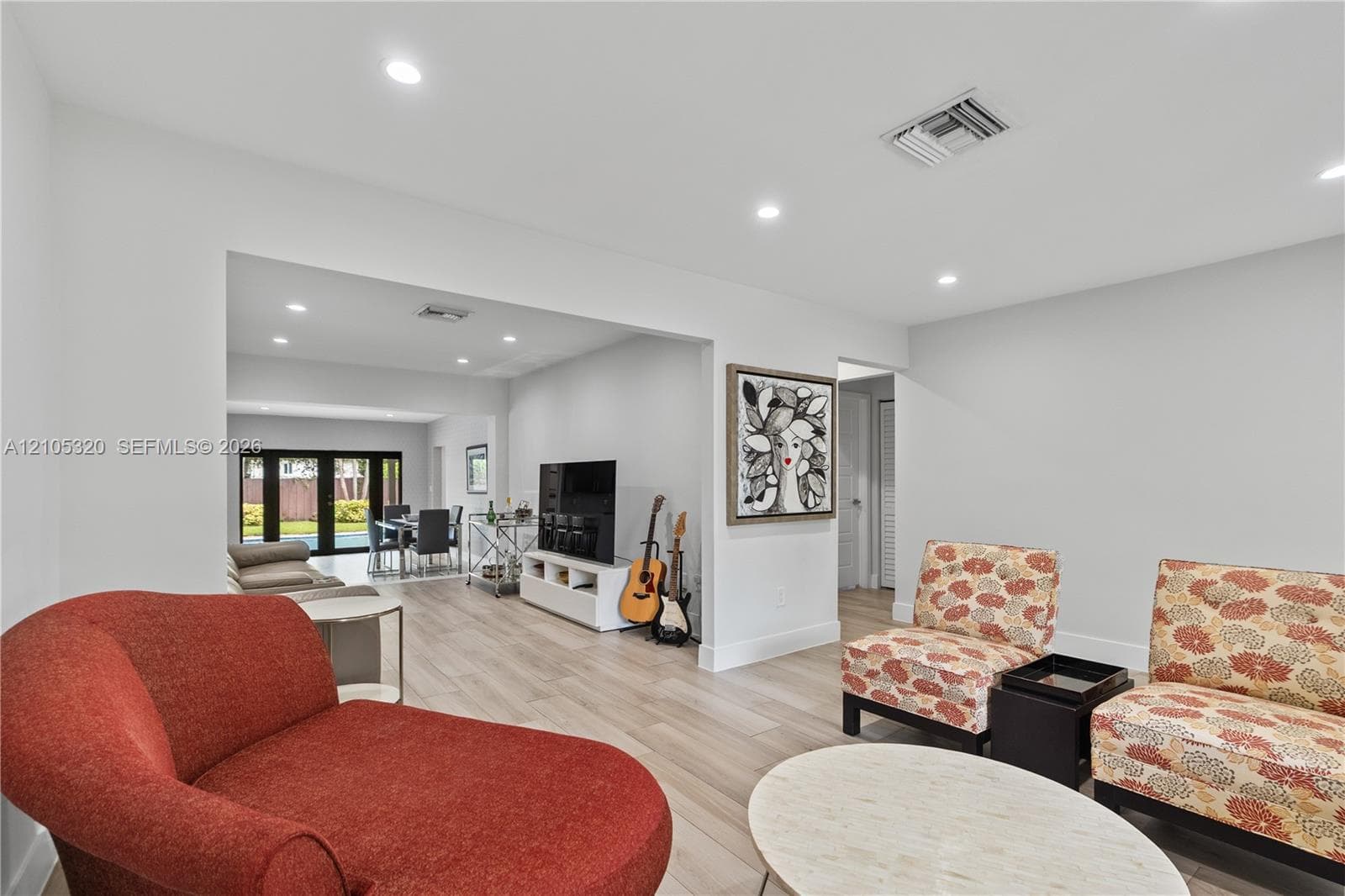 Open-concept living area with light-toned wood-finish flooring, recessed lighting, and white walls