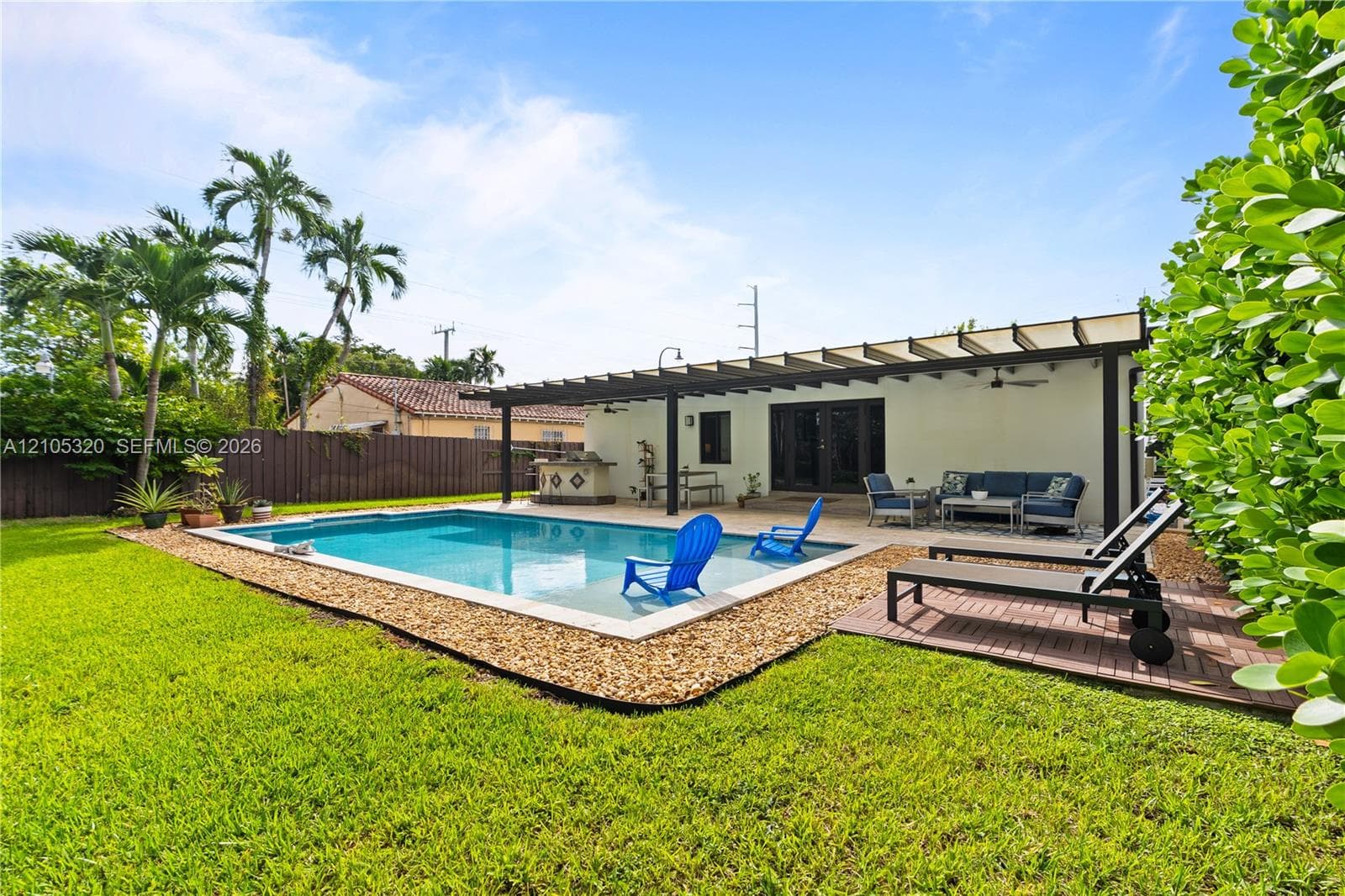 Expansive backyard featuring a rectangular swimming pool, an attached pergola, a built-in outdoor kitchen, a paved patio, and a manicured lawn