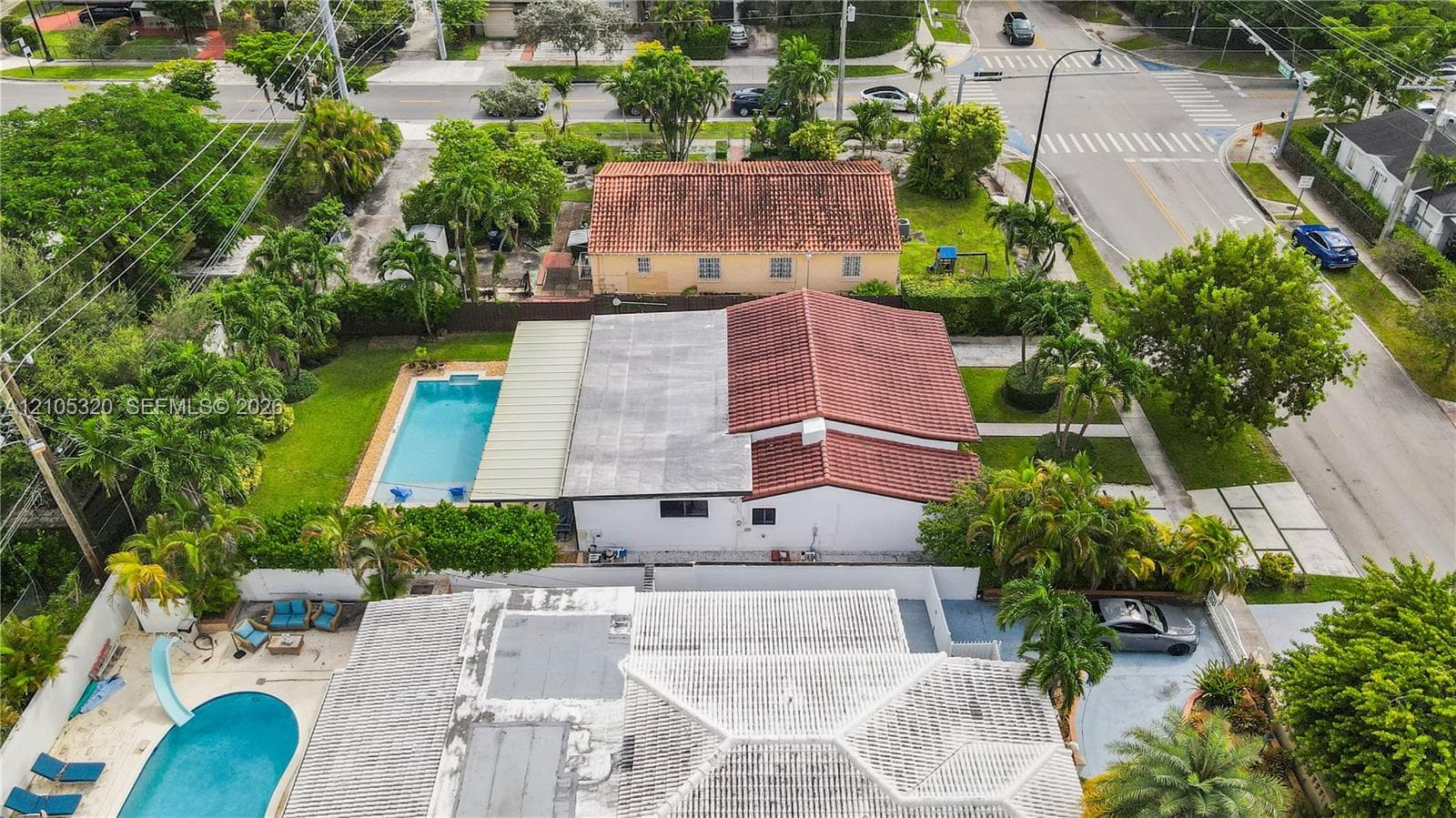 Rectangular swimming pool with surrounding lawn, mature landscaping, and an adjacent structure featuring a red tile roof
