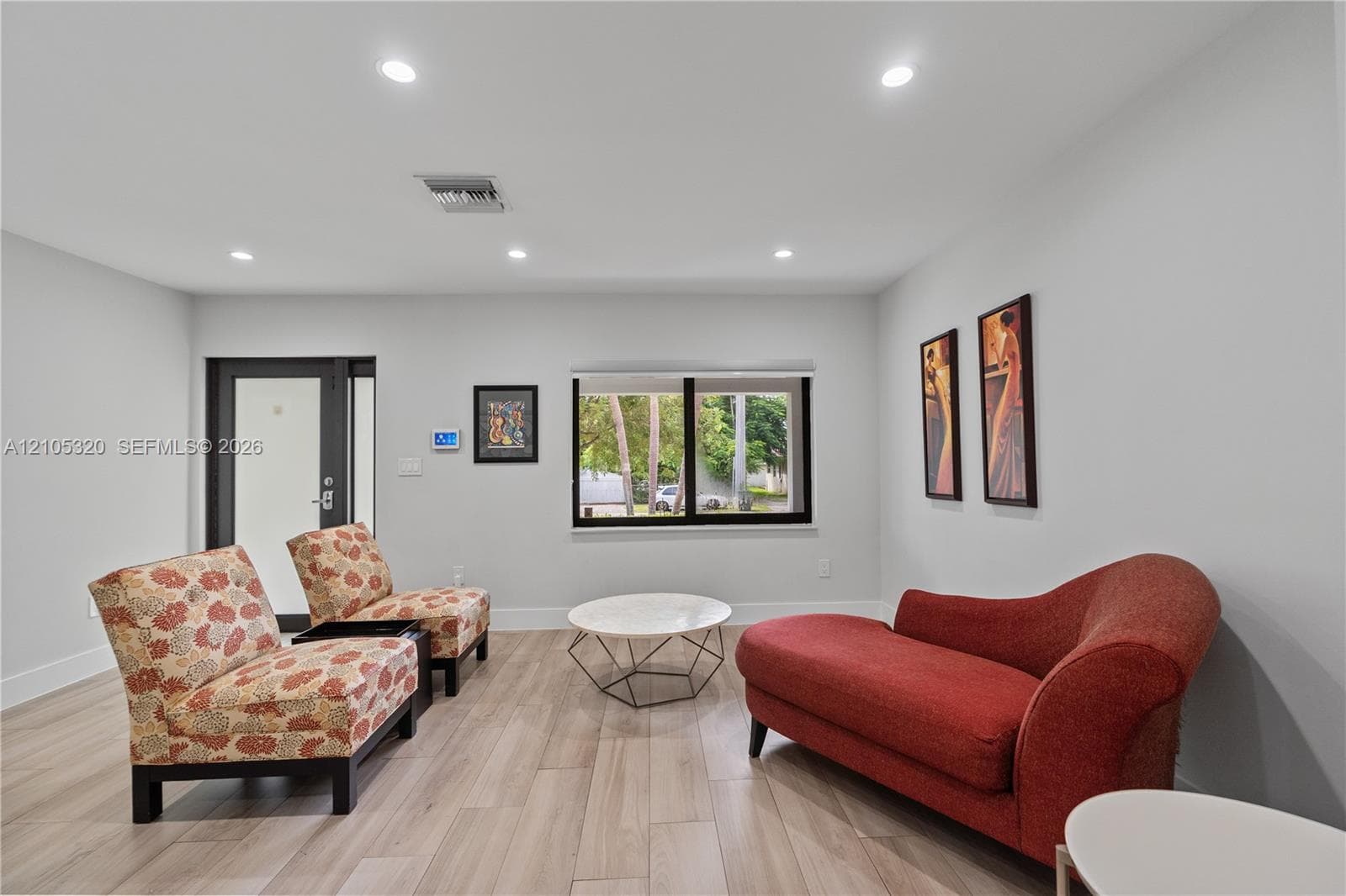 Recessed lighting illuminating the room, light-toned wood-finish flooring, and a window with black trim