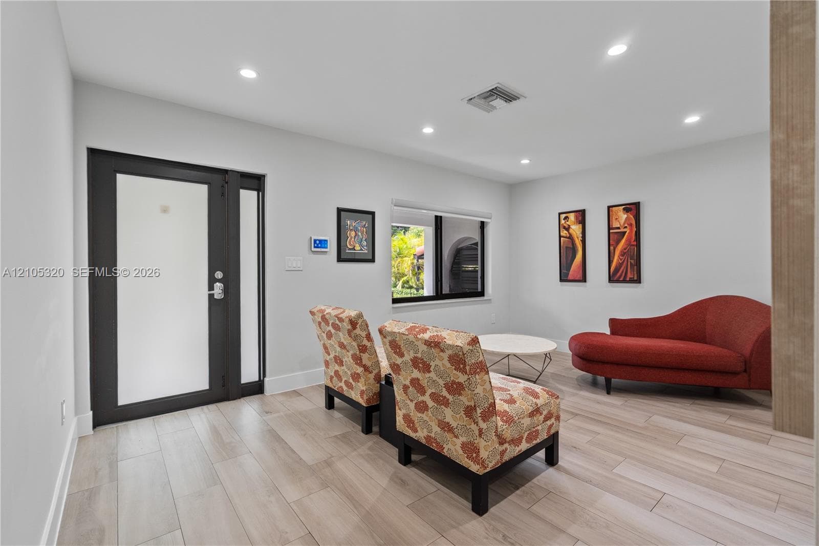 Recessed lighting illuminates the space, featuring plank-style flooring and a dark-framed entry door with a frosted glass panel