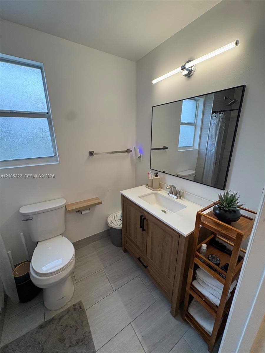 White vanity with integrated sink, modern black-framed mirror, contemporary wall-mounted light fixture, and large format tile flooring