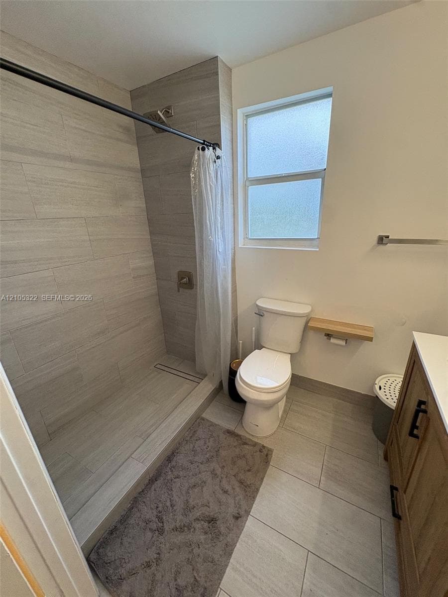 Tiled shower with a linear drain, light wood-finish vanity, and a window with privacy glass