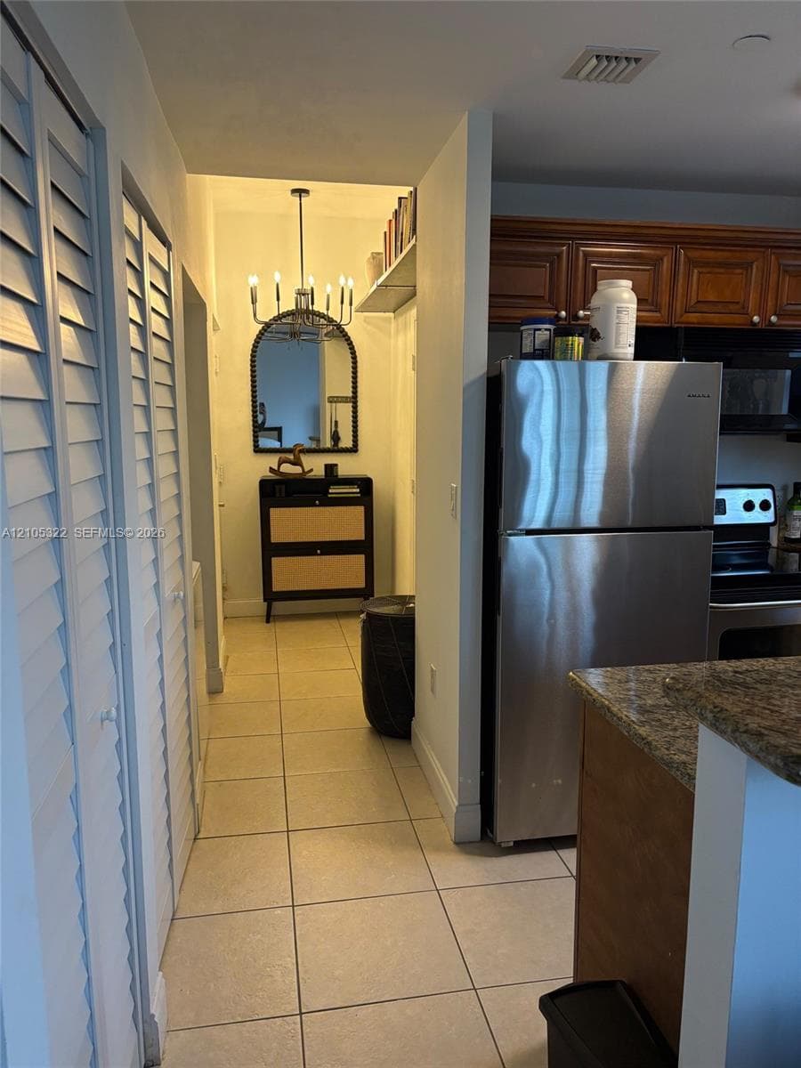 Tile flooring, built-in shelving, white louvered closet doors, and a decorative chandelier