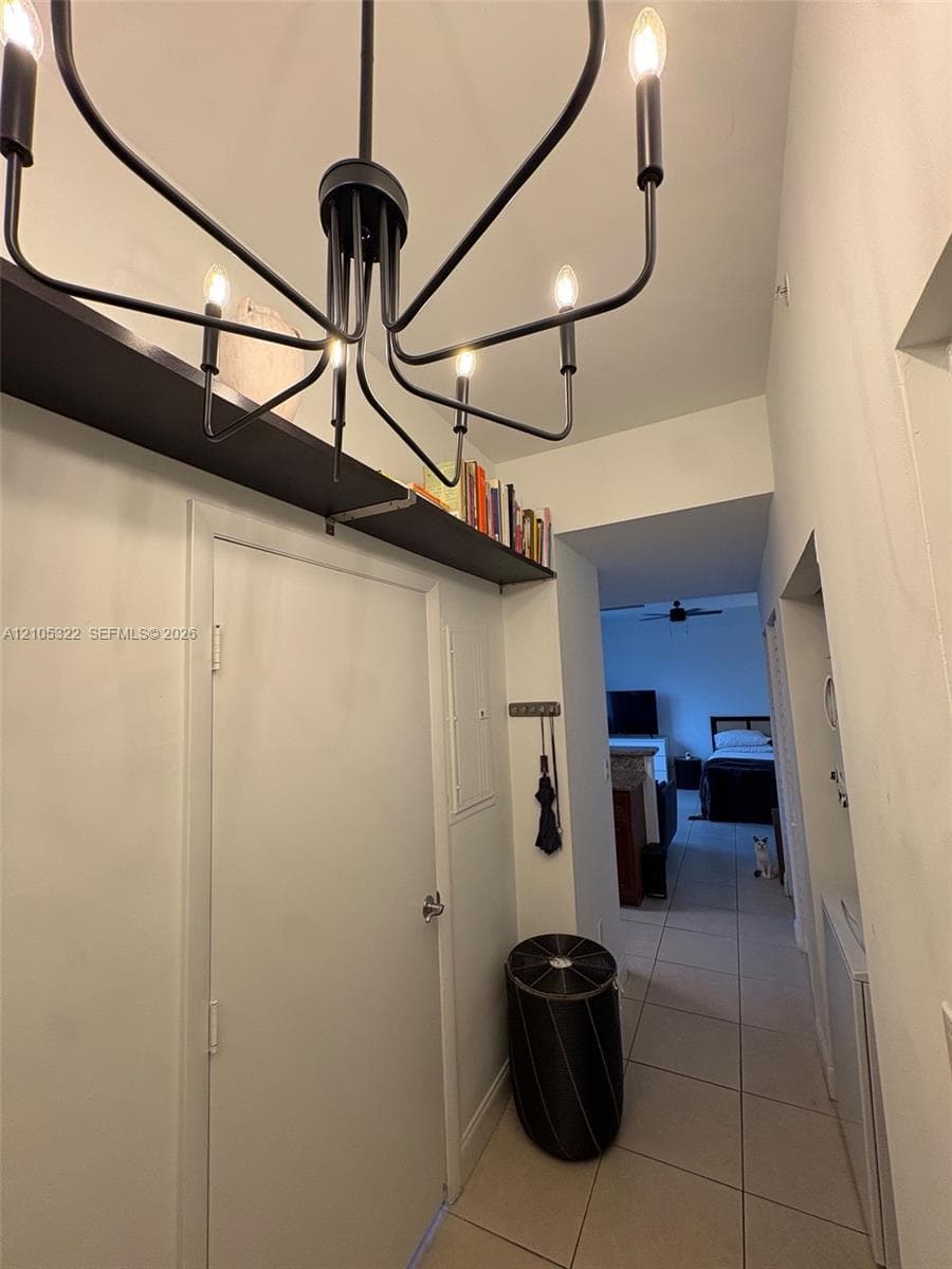 Recessed ceiling with a contemporary black chandelier, built-in wall shelving, and tile flooring