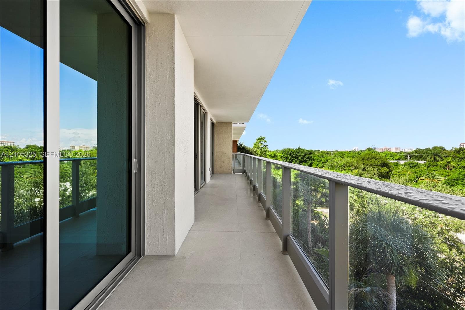 Expansive private balcony with full-length glass railing, concrete flooring, and multiple sliding glass doors