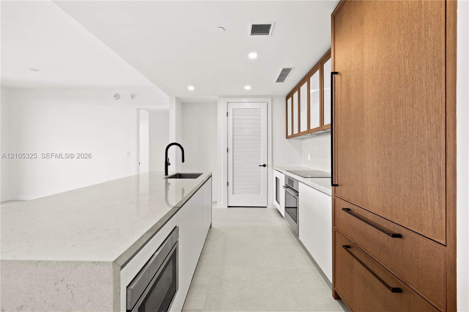 Kitchen featuring an integrated microwave, flat-panel wood-finish cabinetry, white countertop, and a black gooseneck faucet