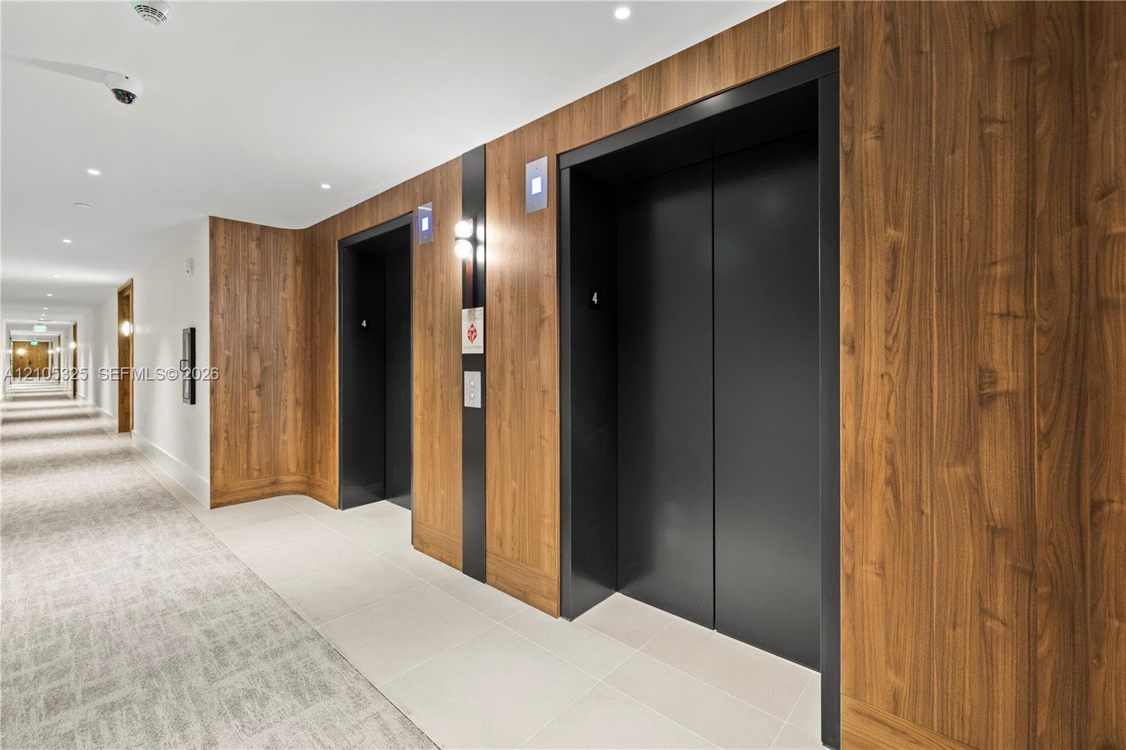 Hallway featuring wood-finish wall panels, recessed lighting, and elevators with black doors