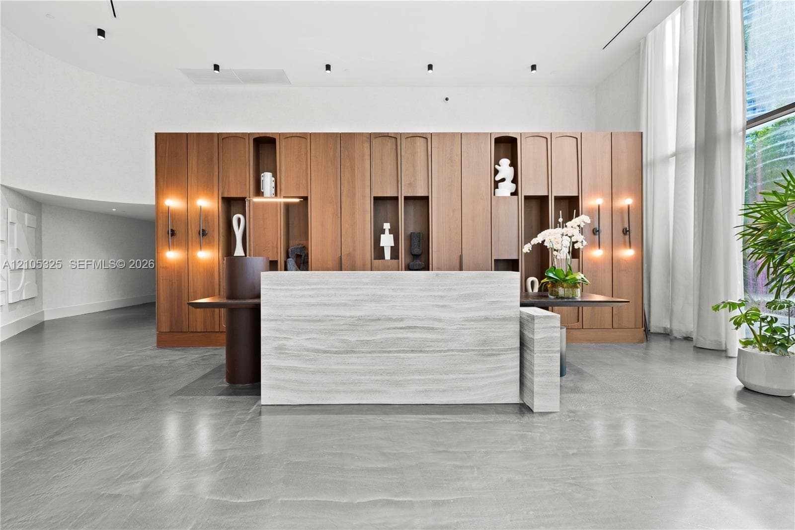 Stone-clad reception desk, wood-paneled wall with integrated shelving, wall-mounted sconces, recessed ceiling lighting, and expansive floor-to-ceiling windows