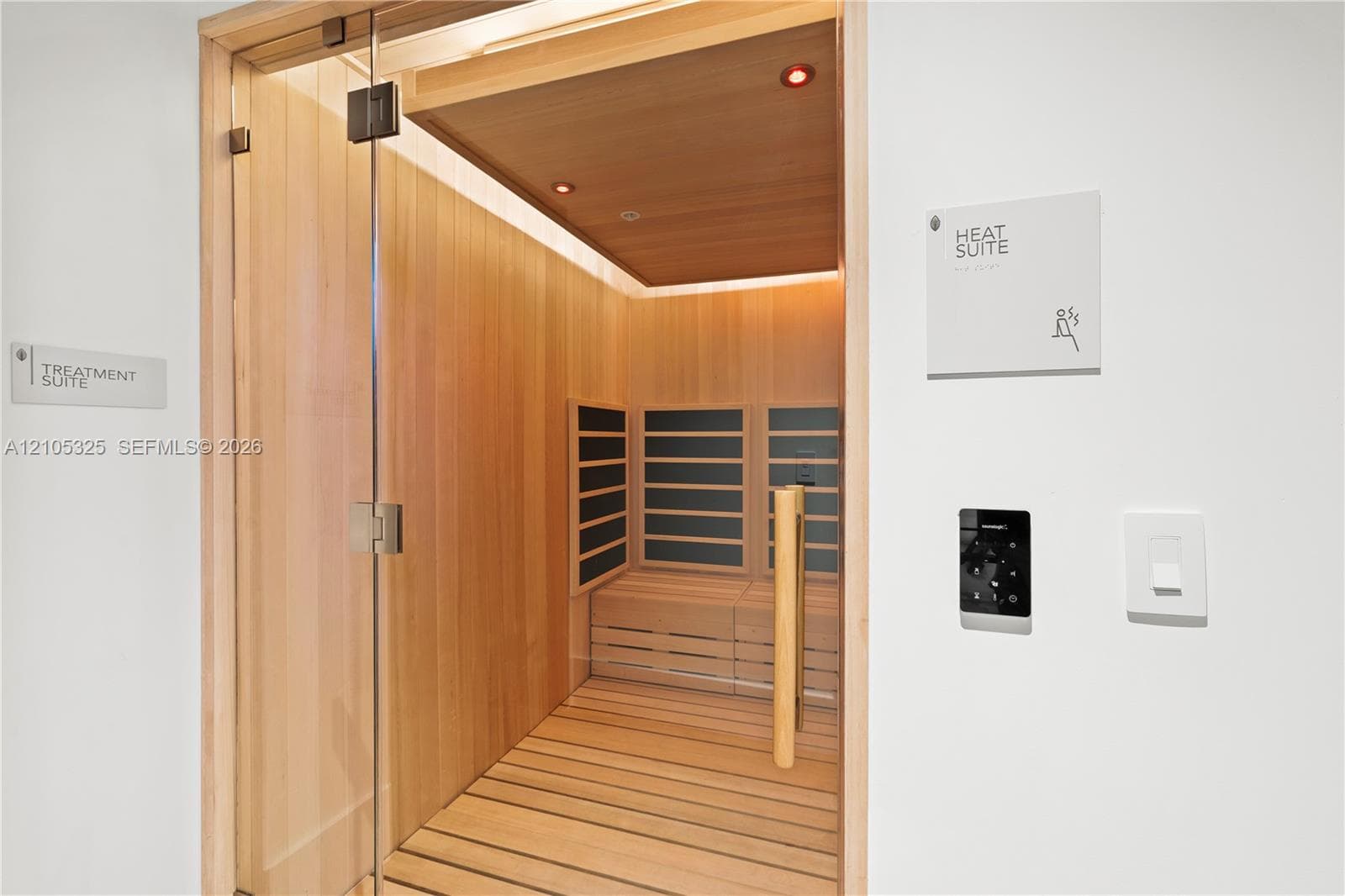 Wood-paneled heat suite featuring a glass door, built-in wooden bench, and integrated wall controls