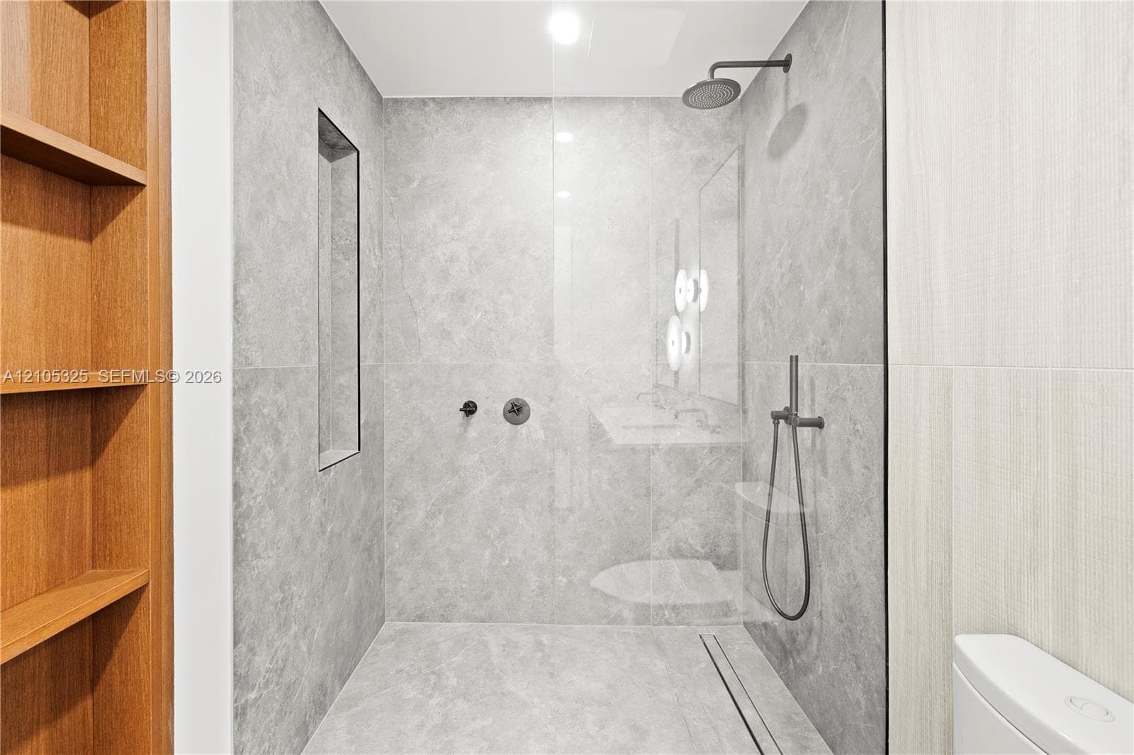 Glass-enclosed shower with matte black fixtures, integrated wall niche, and light gray tiled walls