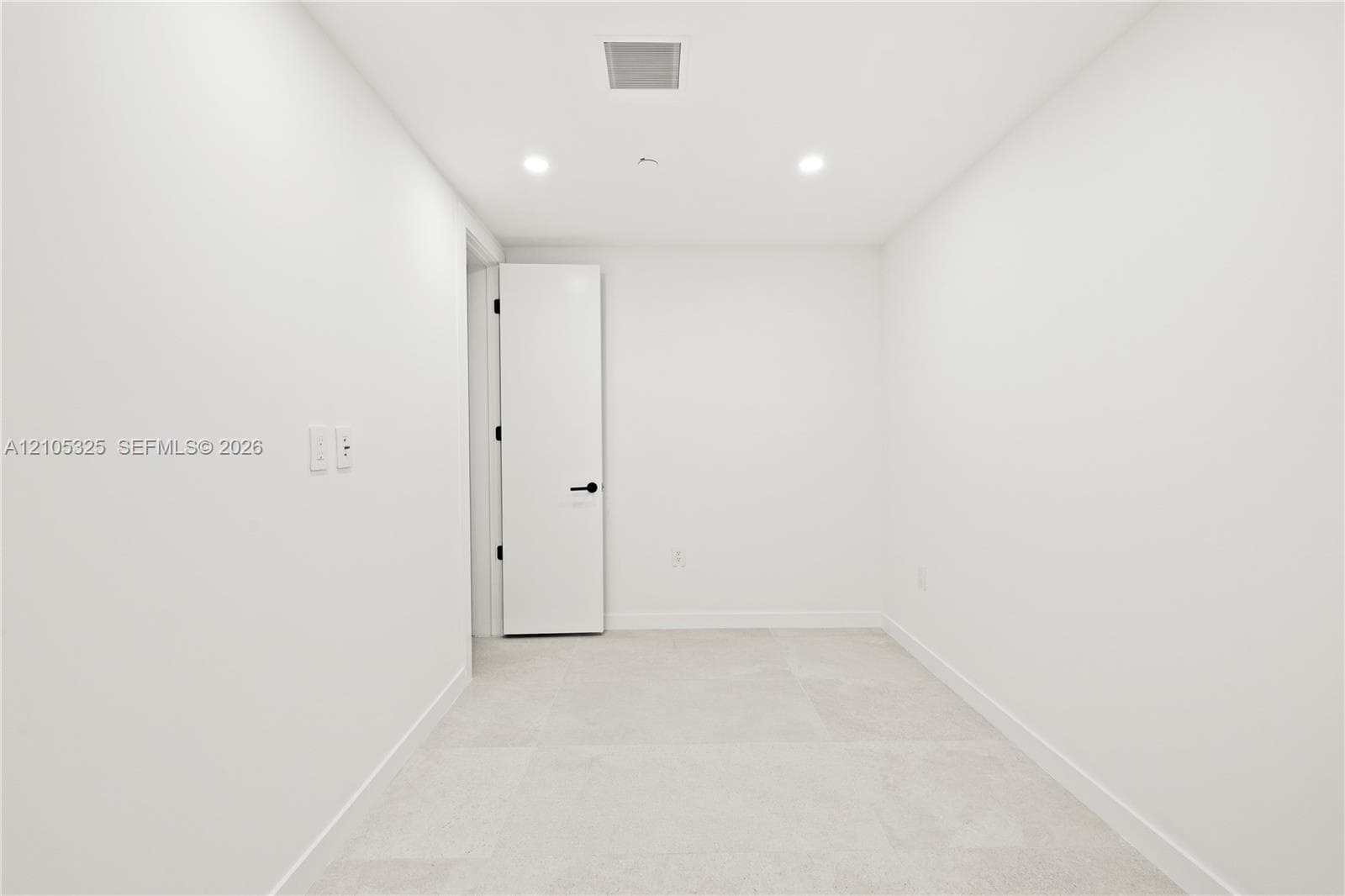 Recessed ceiling lighting, white walls, light-colored tile flooring, solid core door with matte black hardware